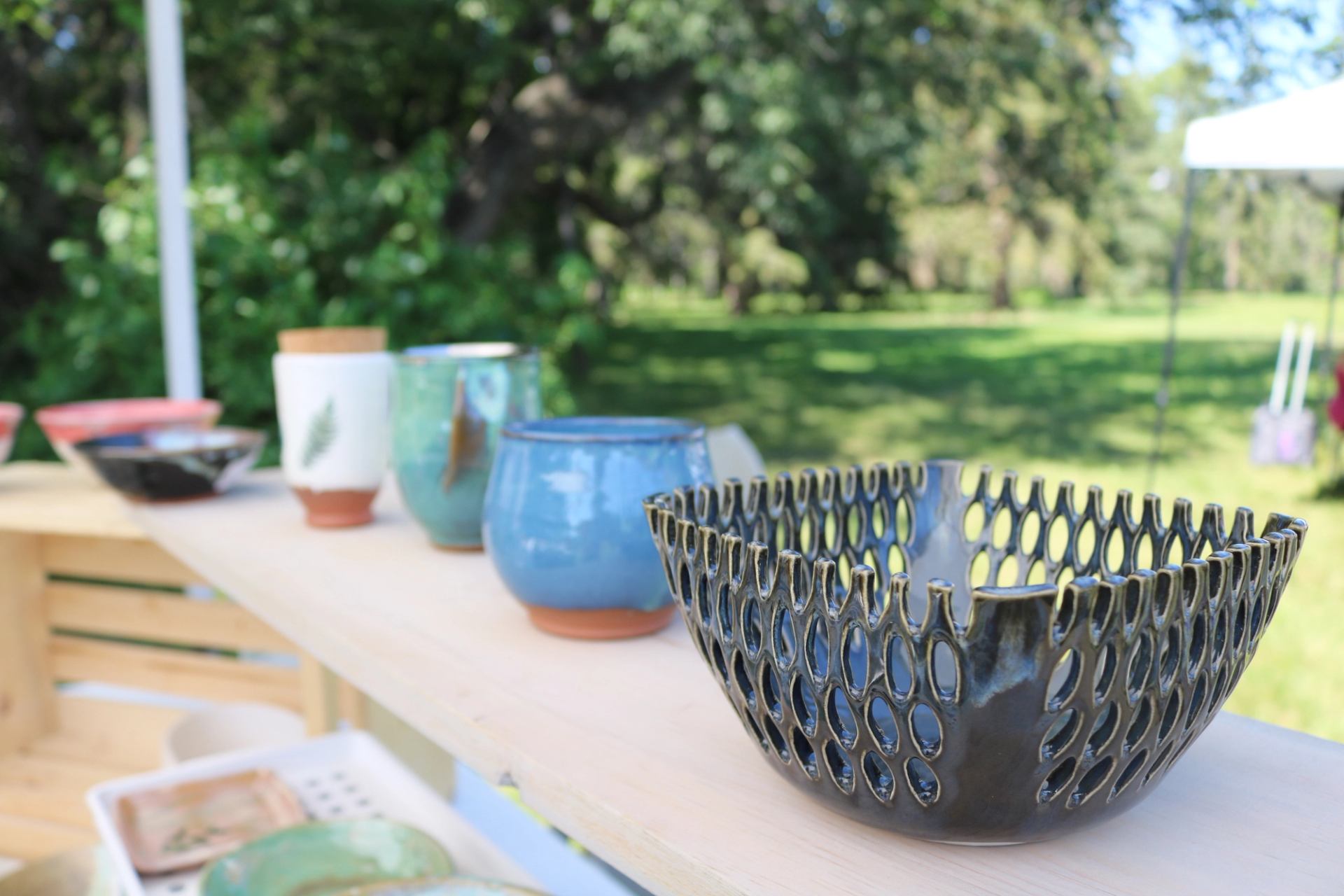 Handmade pottery pieces displayed on a wooden shelf at an outdoor market.