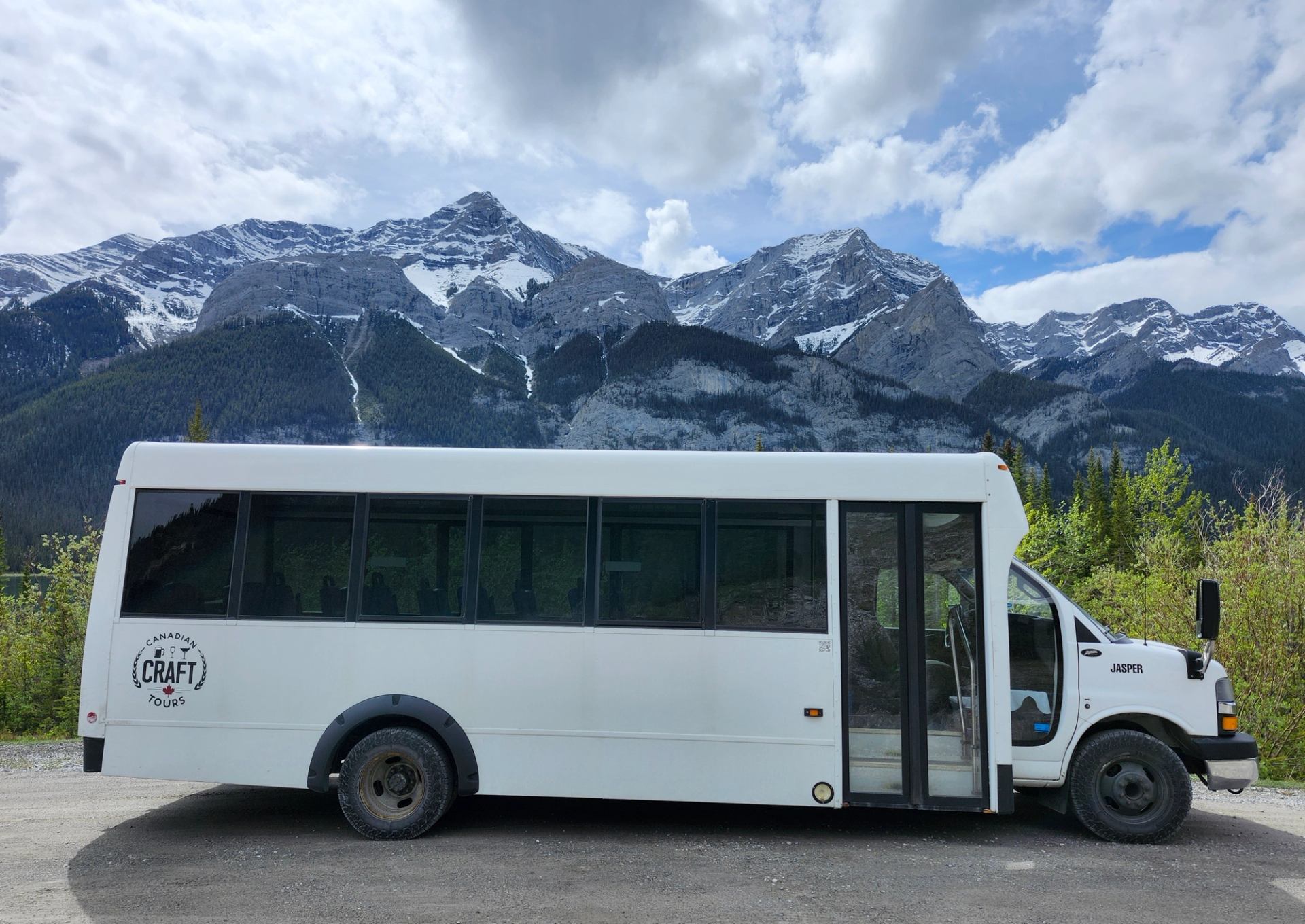 White tour bus in foreground with Canadian Rockies mountains and snow patches in background.