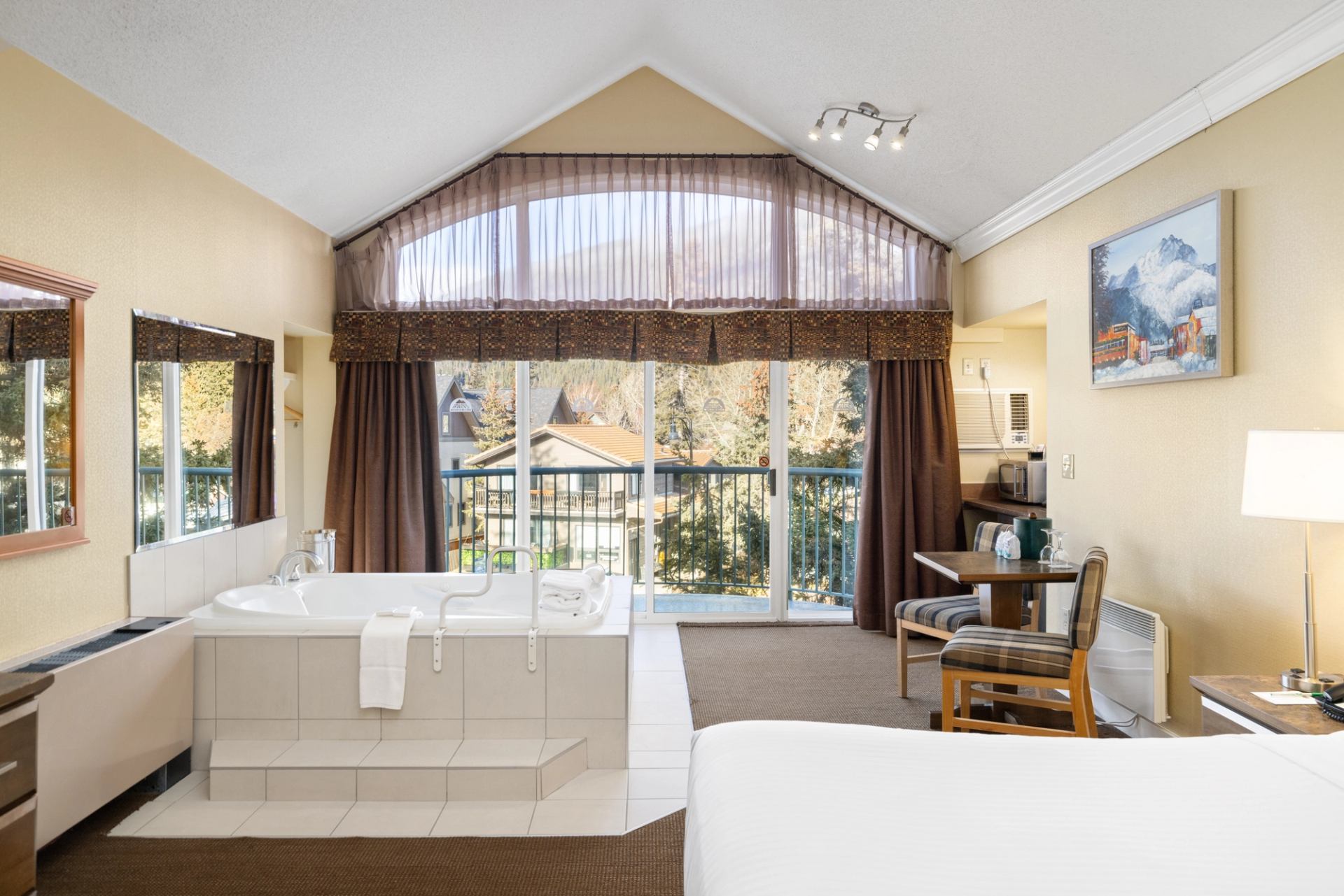 Hotel room with jacuzzi tub, seating area, and large windows with sheer curtains.