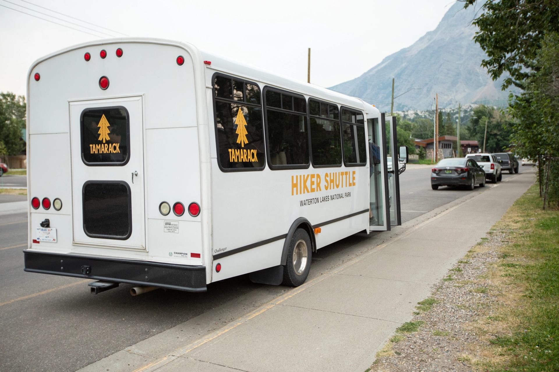 Tamarack hiker shuttle parked curbside in Waterton with mountains in the distance.