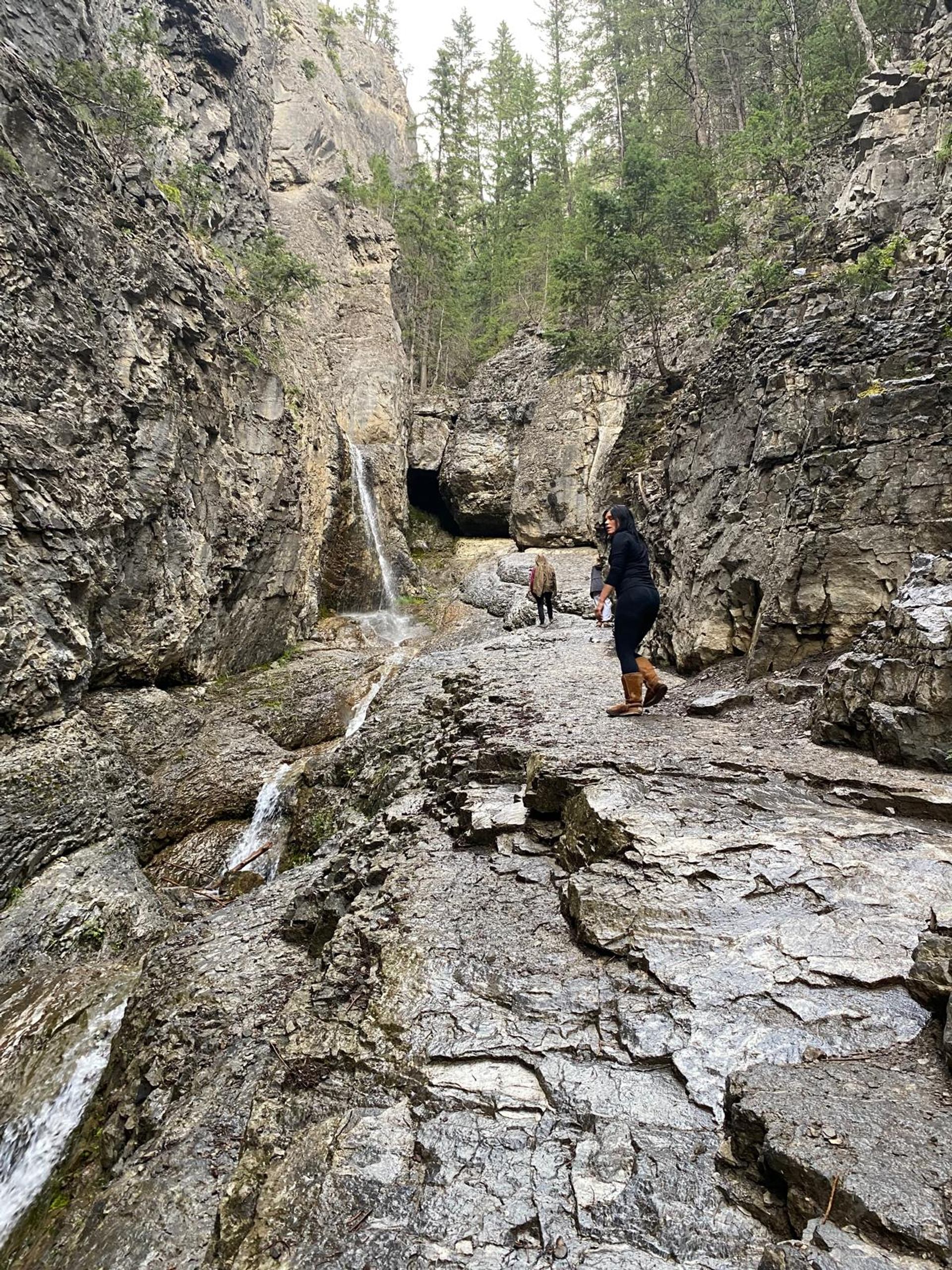 Visitors explore a rugged canyon featuring a small waterfall, rocky terrain, and evergreen trees.