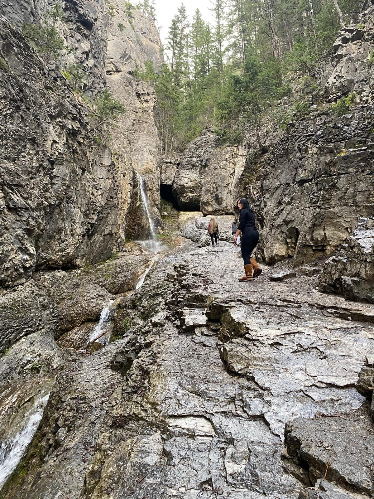 Visitors explore a rugged canyon featuring a small waterfall, rocky terrain, and evergreen trees.