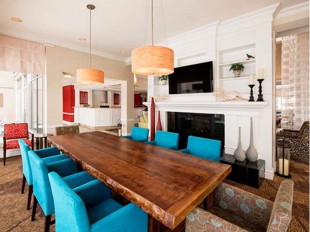 Modern Hilton Garden Inn lounge with wood table, blue chairs, and fireplace.