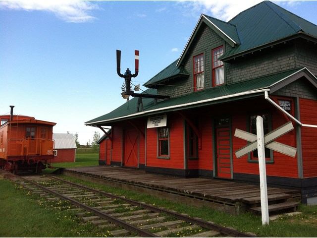 Red wooden train station building with rail tracks and museum display sign.