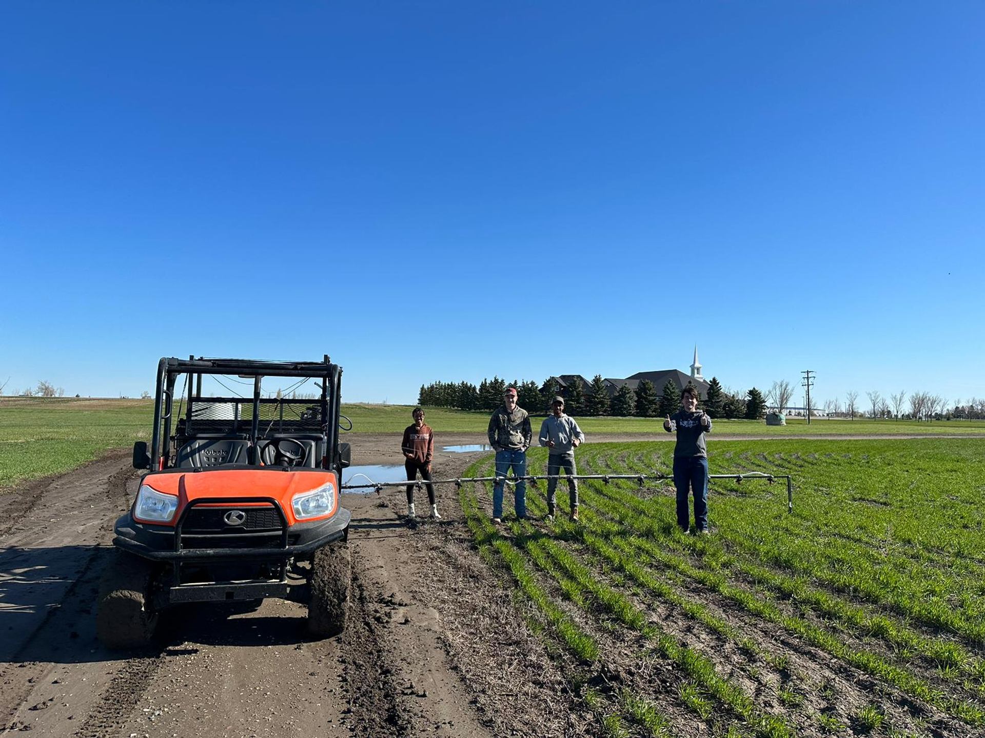 Farm vehicle and four people standing beside irrigation equipment in a green field.