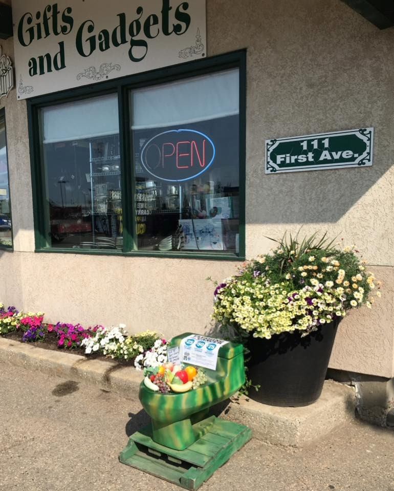 Gifts and Gadgets storefront with open sign, street address plaque, and flower planters outside.