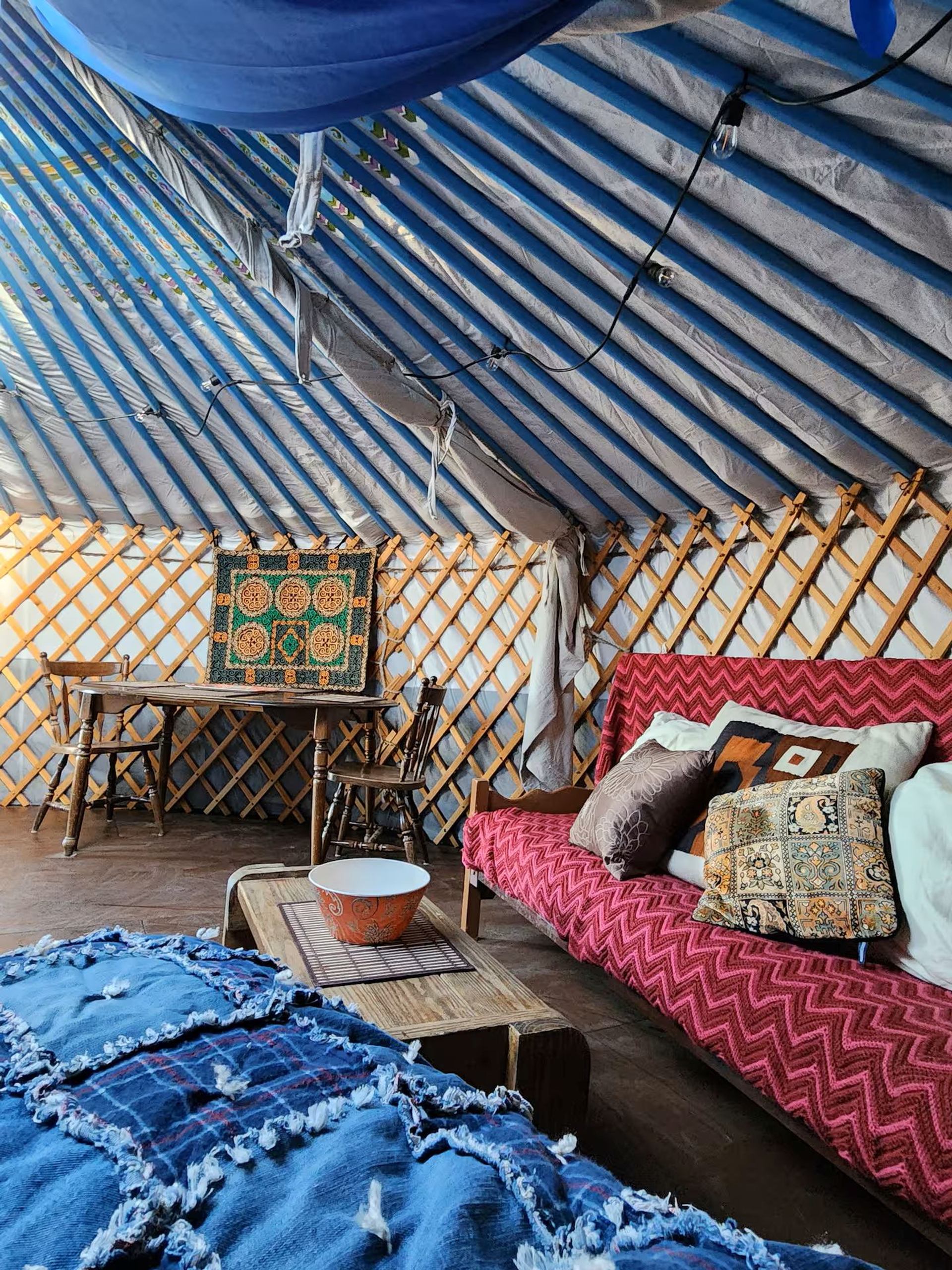 Interior view of yurt with a red couch, table, blue quilt, and lattice walls.