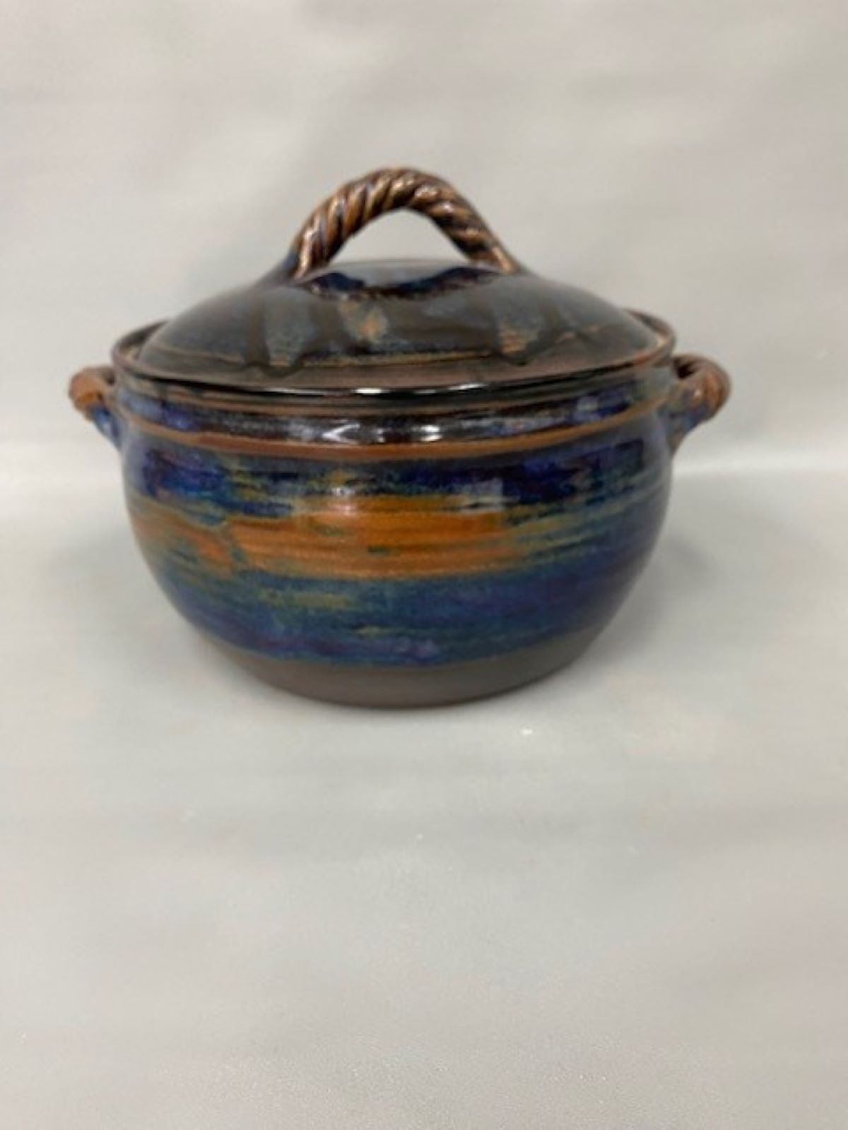 Handcrafted lidded ceramic pot with blue and earthy brown glaze on a light background.