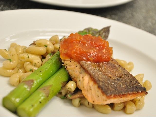Seared salmon on pasta with asparagus and red sauce, plated elegantly.