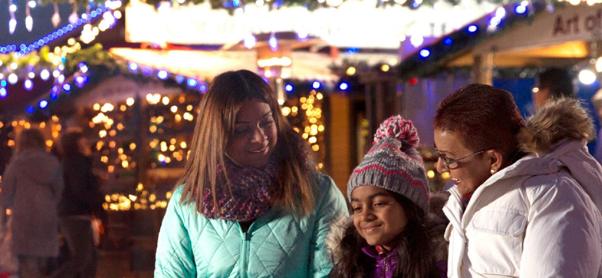 Visitors in winter coats walking through brightly lit Enchanted Festival  at night.
