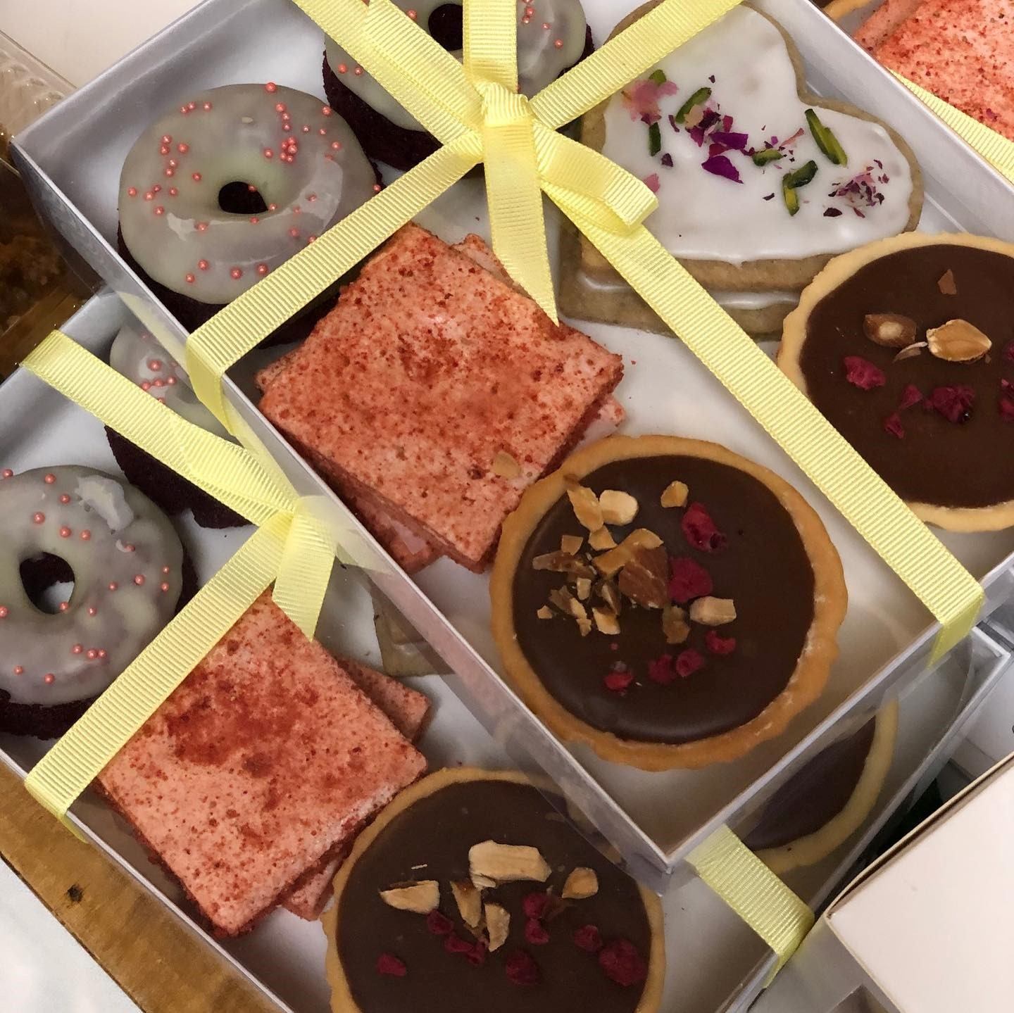 Box of decorated donuts and pastries tied with a yellow ribbon, with two slices visible.