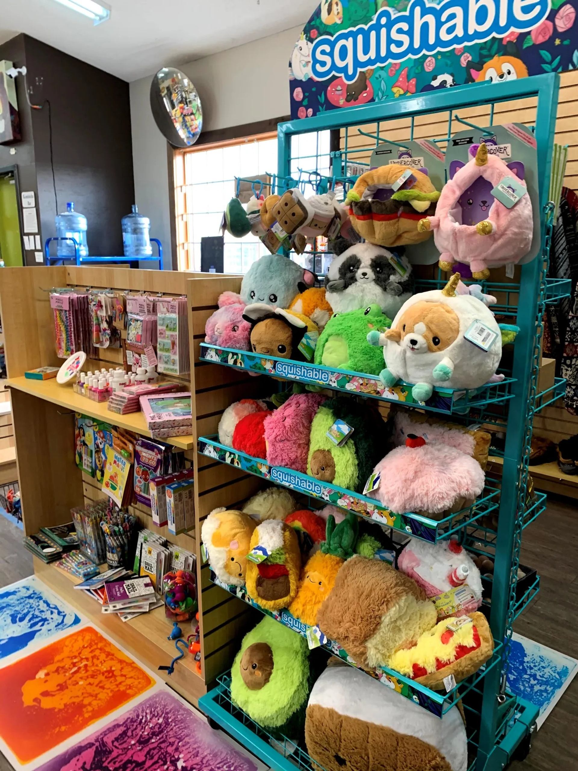 Store display of Squishable plush toys beside craft supplies and colourful sensory floor mats.