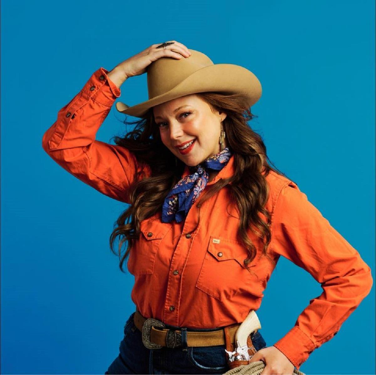 Kaitlin Butts wearing a cowboy hat and red western shirt with a pistol on her side.