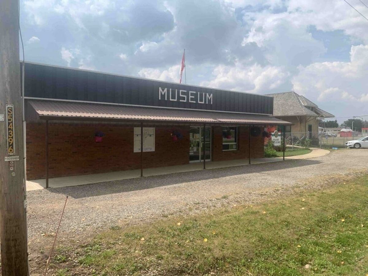 Small brick museum building with front awning, gravel driveway and Canadian flag above.