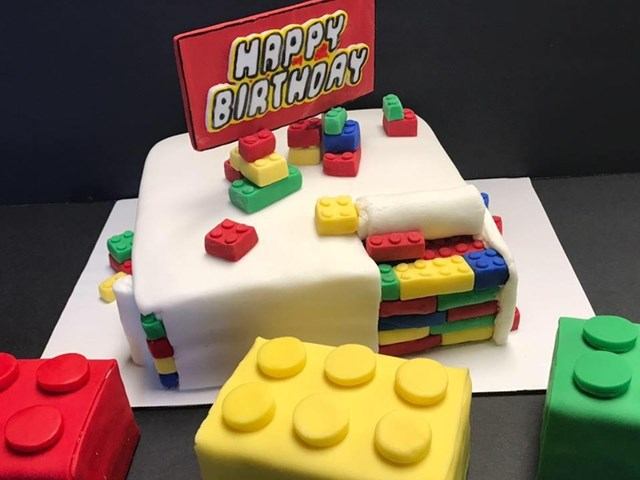 White birthday cake decorated with colorful brick‑style pieces and a “Happy Birthday” topper.