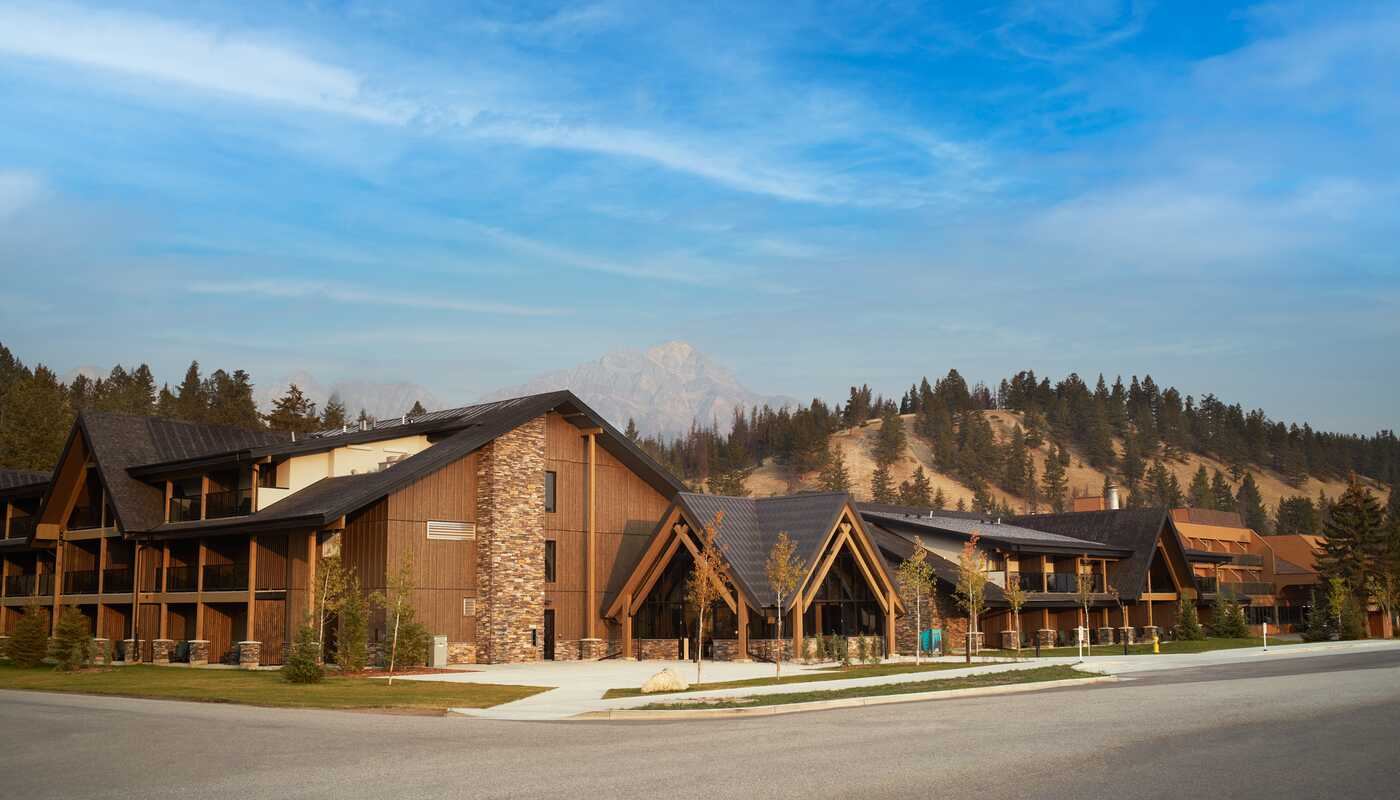Lodge-style hotel building with wood and stone facade, mountains and trees behind.