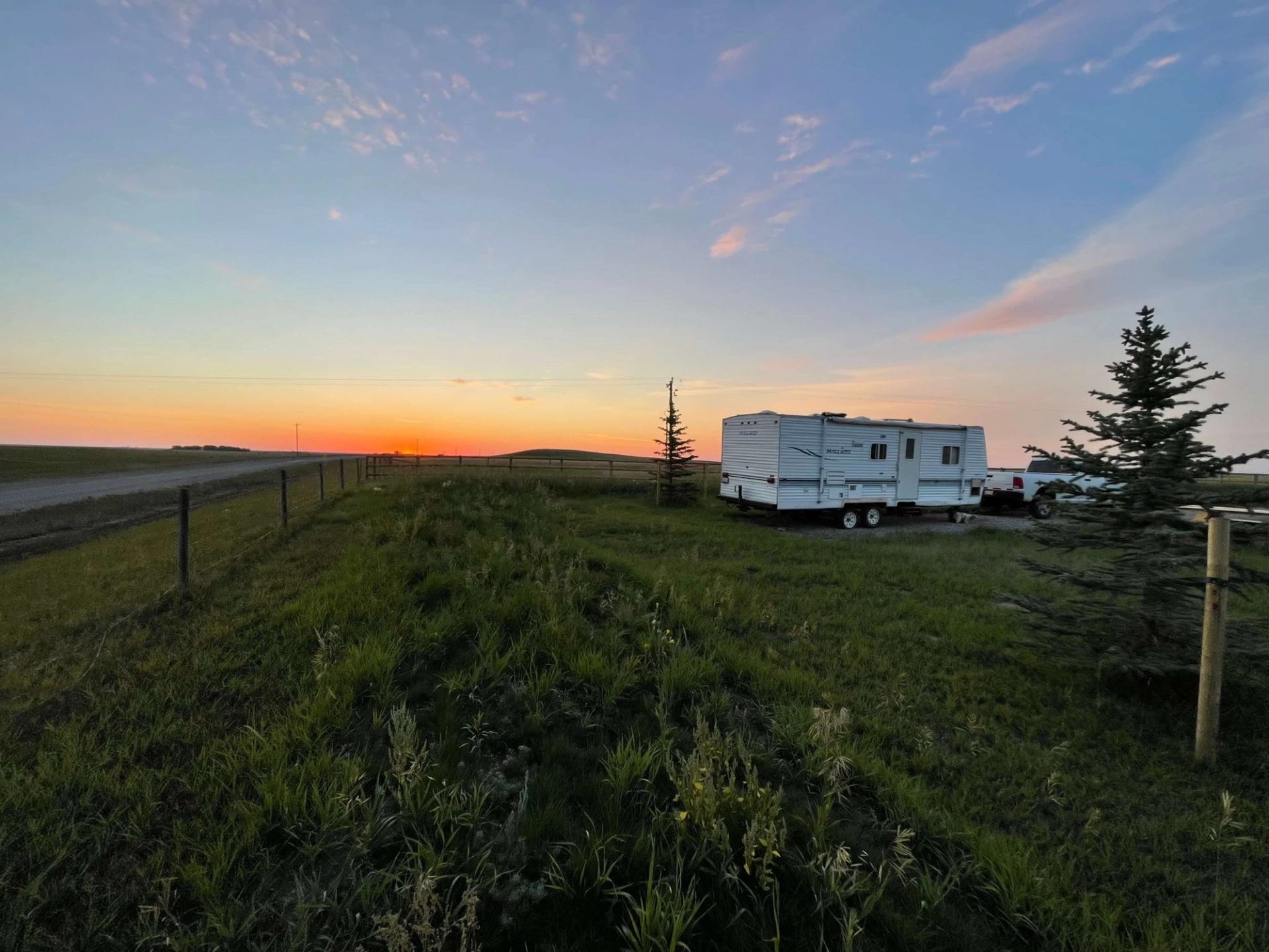 RV parked near trees at sunset in Willow Creek Campground with fence and open road.