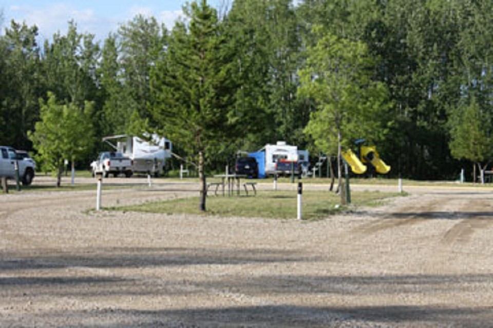 RVs parked near trees with picnic tables, hookups, and a playground in view.