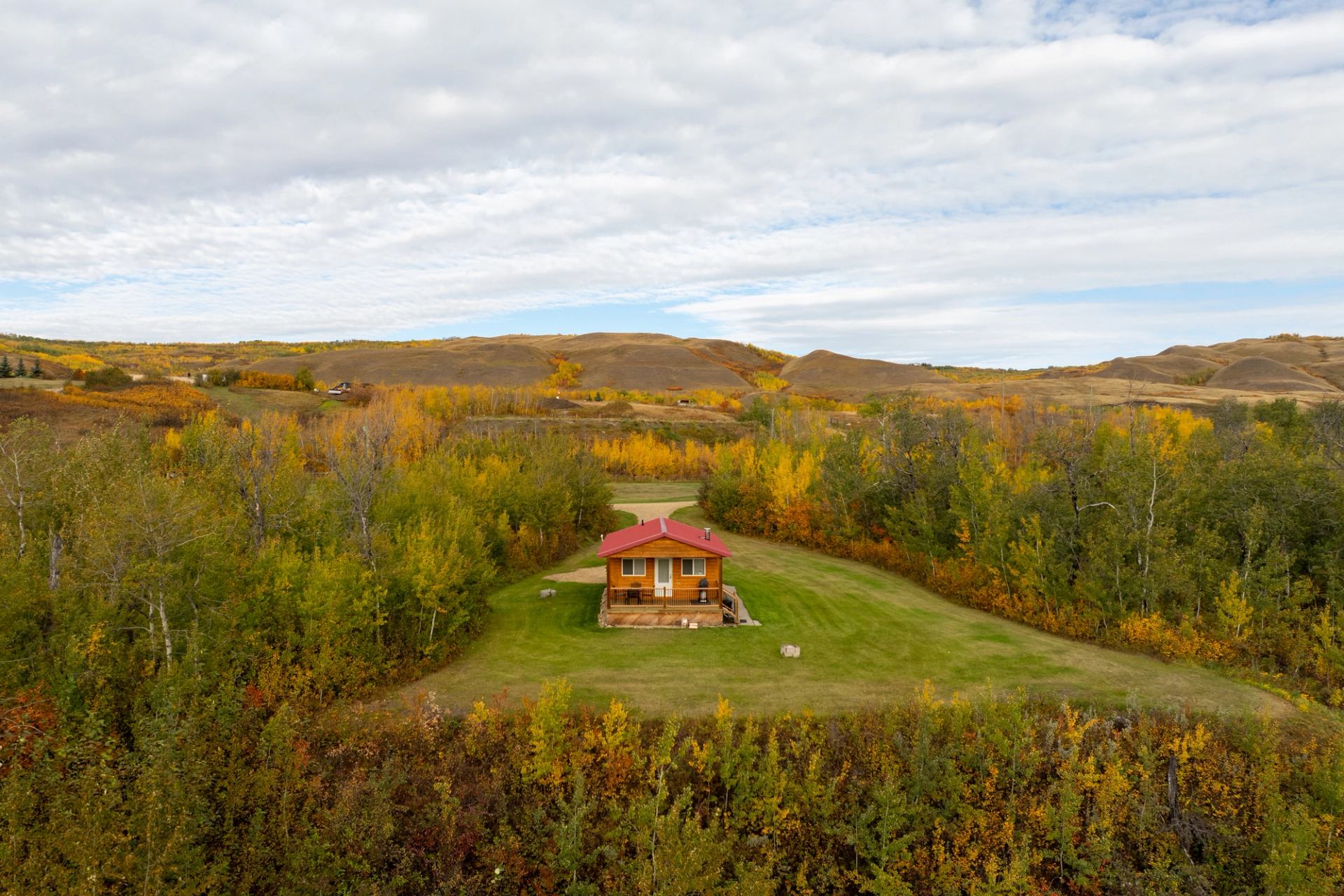 Peace River cabin with red roof, autumn trees, and hills under a cloudy sky in fall.