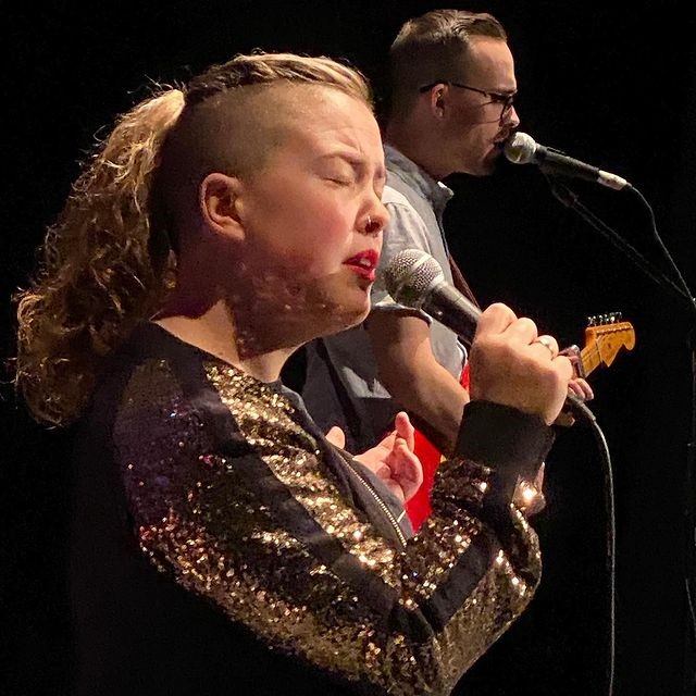 Singer and guitarist performing at a live concert with microphones on stage.