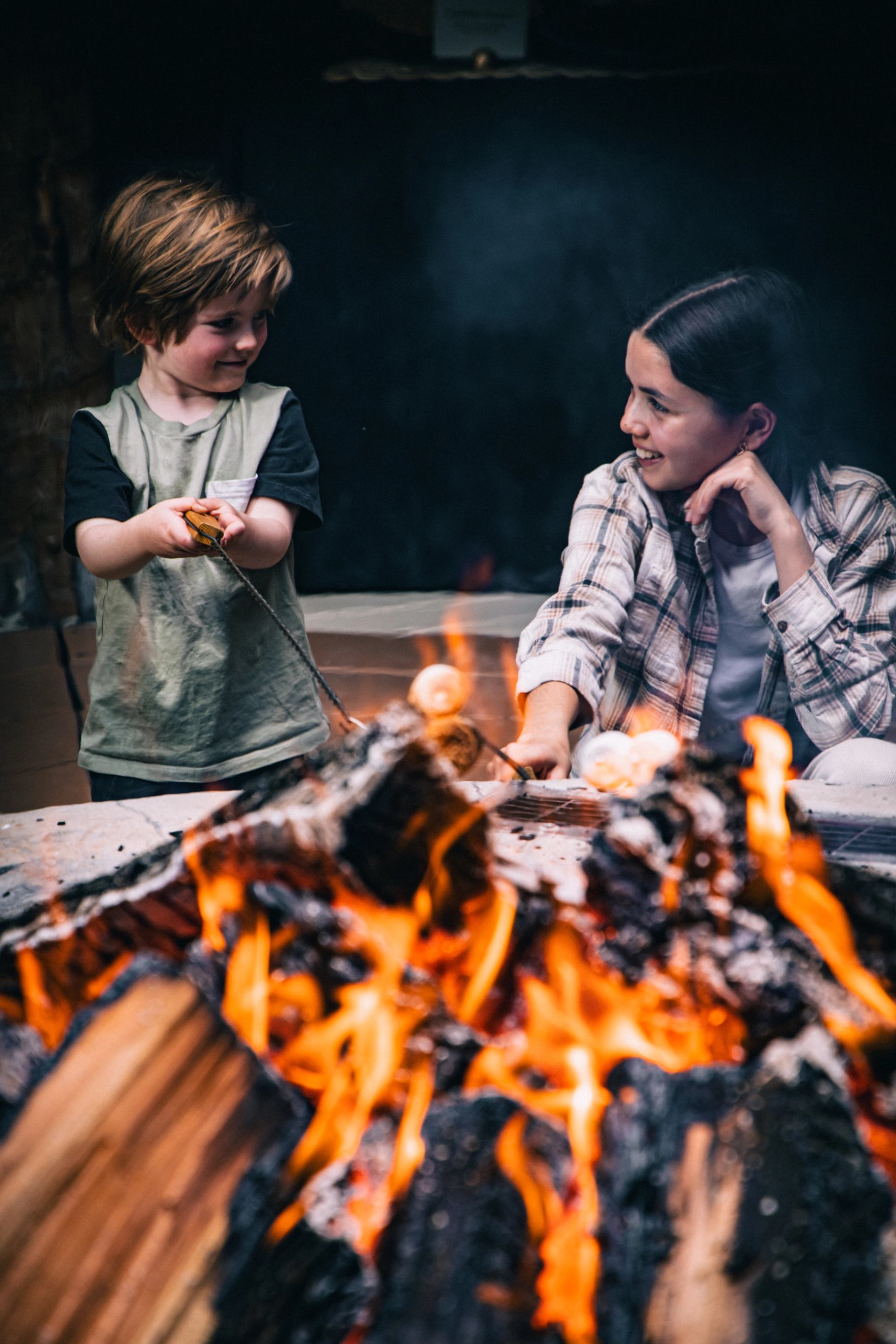 Two people roasting marshmallows over a crackling outdoor fire.
