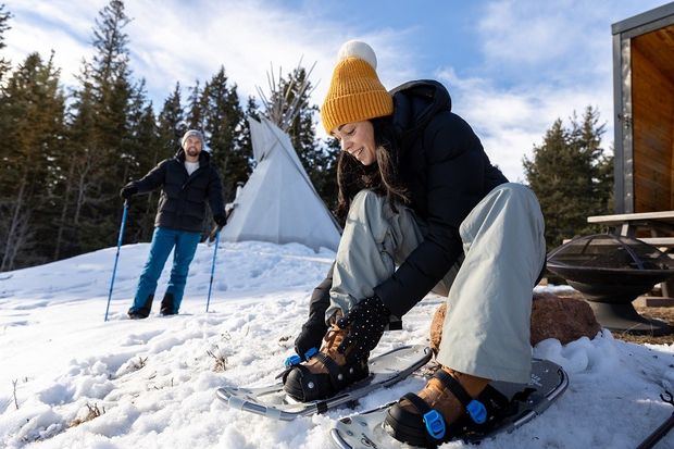 A woman putting on snowshoes with her partner standing nearby.