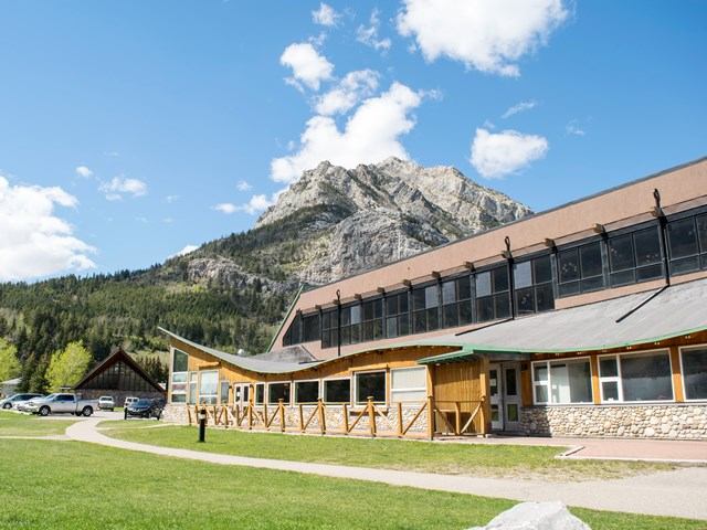 Lodge exterior with mountain backdrop, stone and wood design, and scenic walkway.