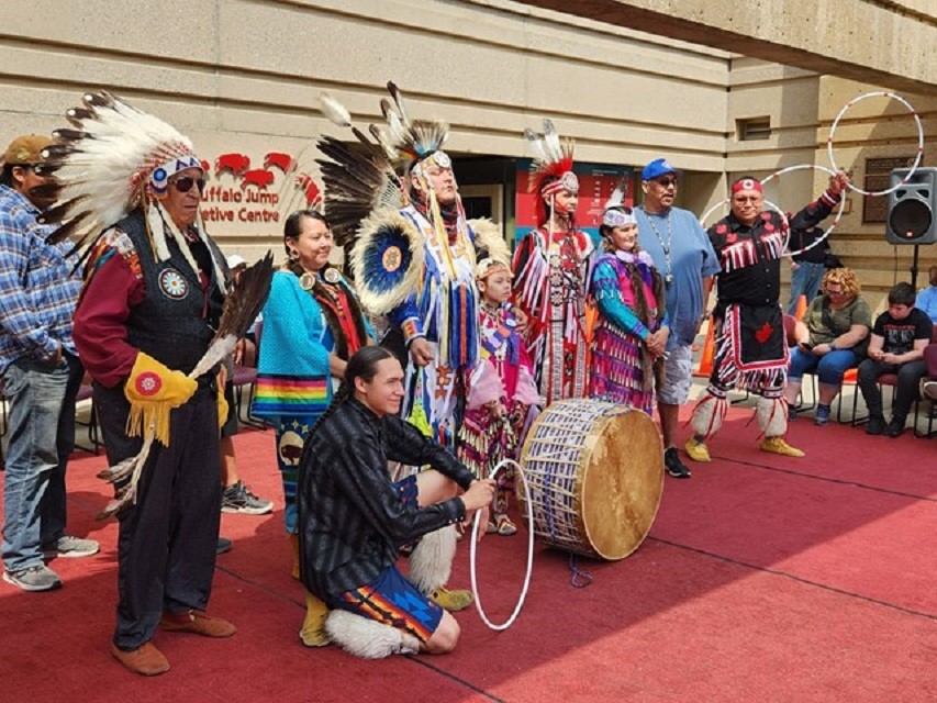 Plaza scene with dancers, drum, and feathered headdresses.