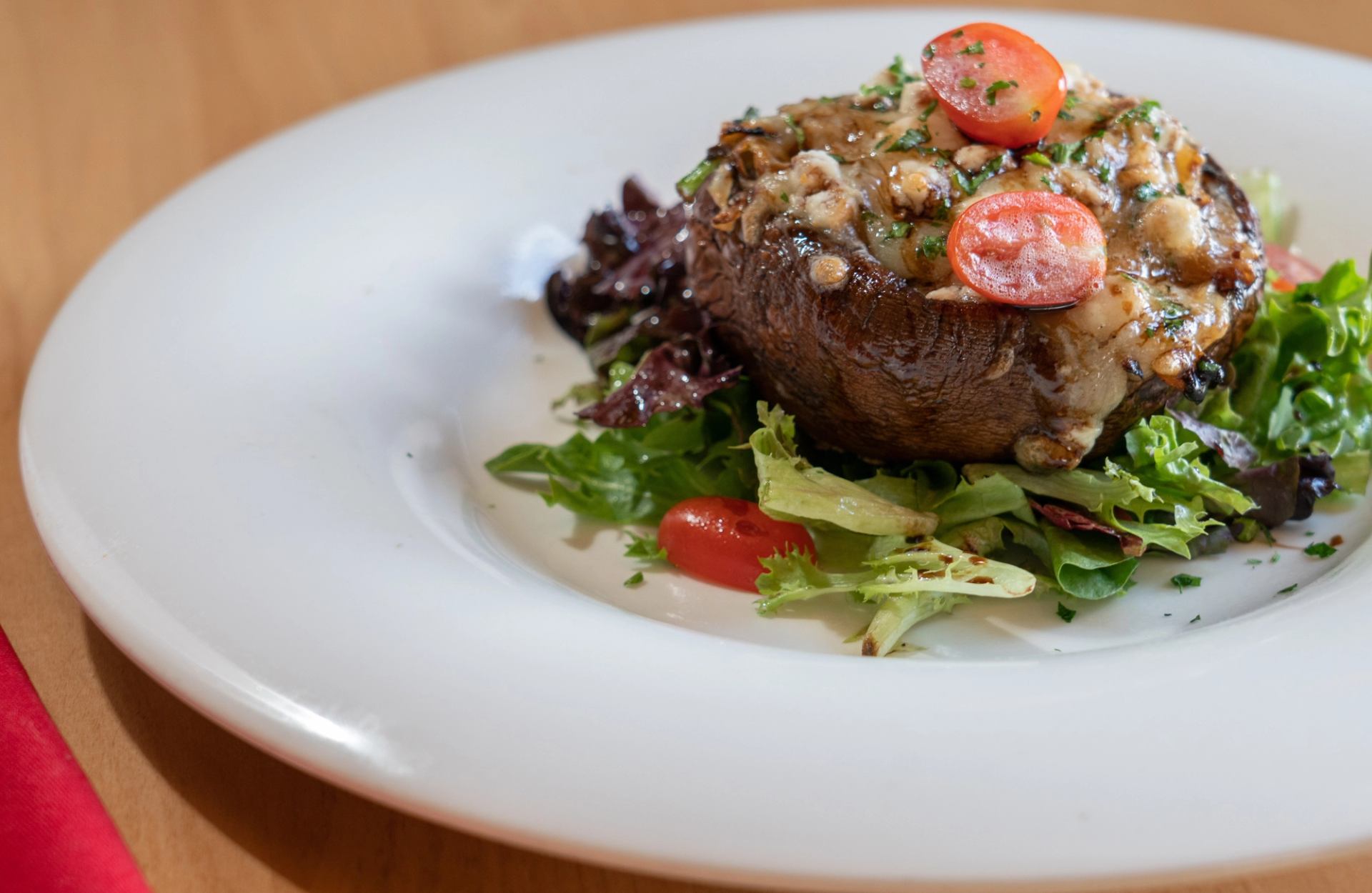 Stuffed mushroom with cheese, herbs, and tomatoes on a bed of greens.