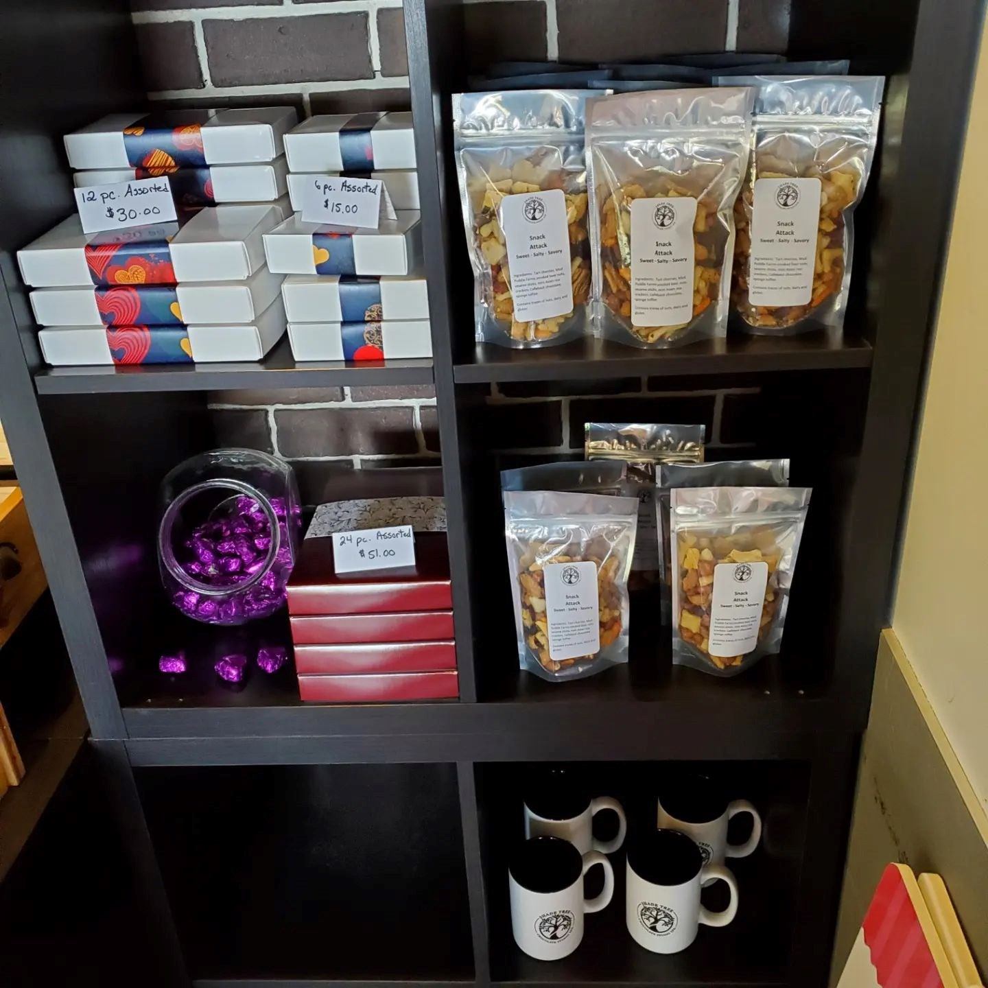 Retail shelf with chocolate boxes, foil snack bags, mugs, and decorative items.