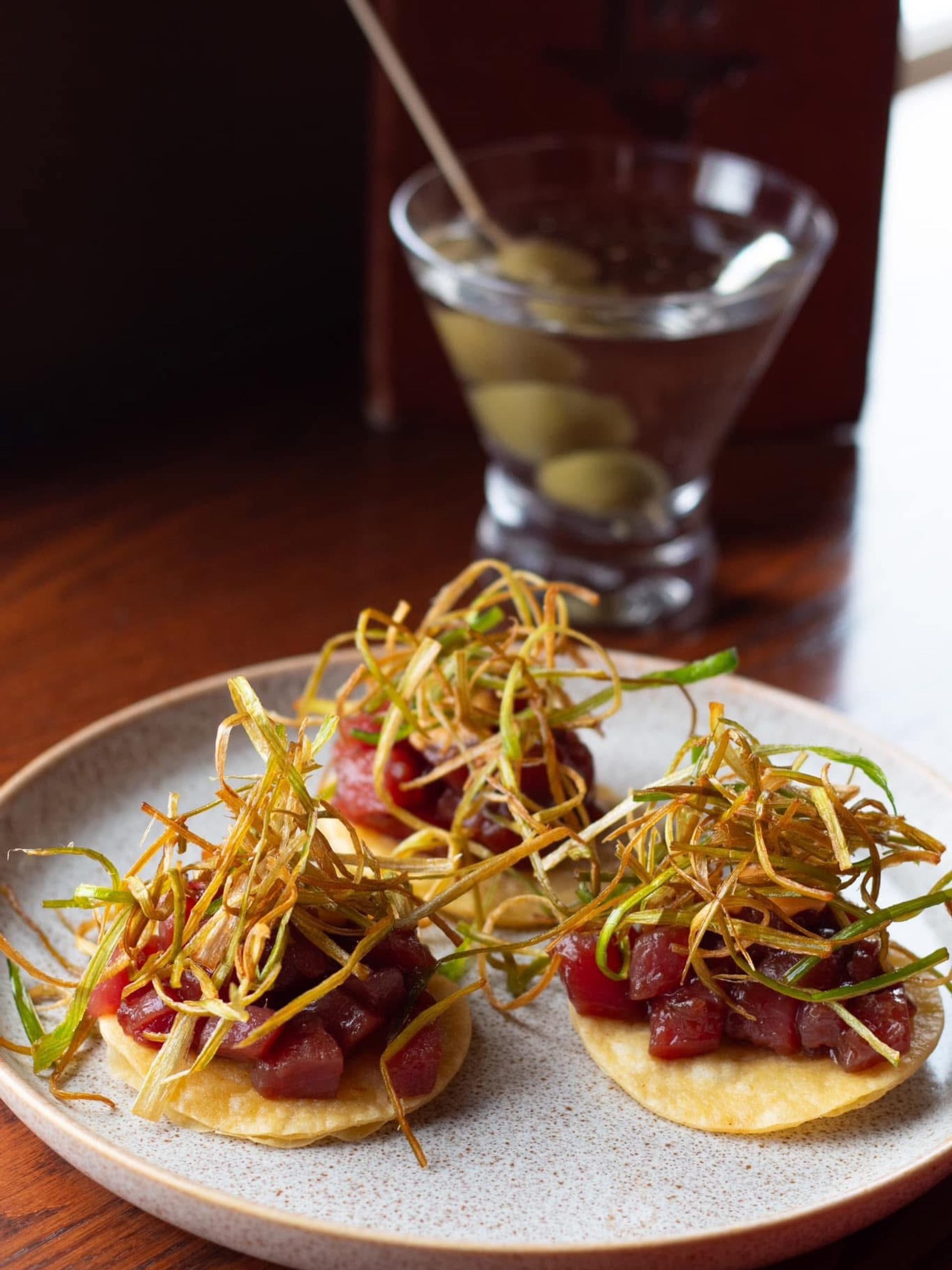 Plate of tuna tartare tostadas with crispy garnish beside a martini with olives.