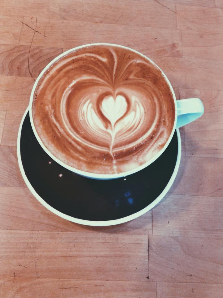 Latte with heart-shaped art in a teal cup on a wooden table.