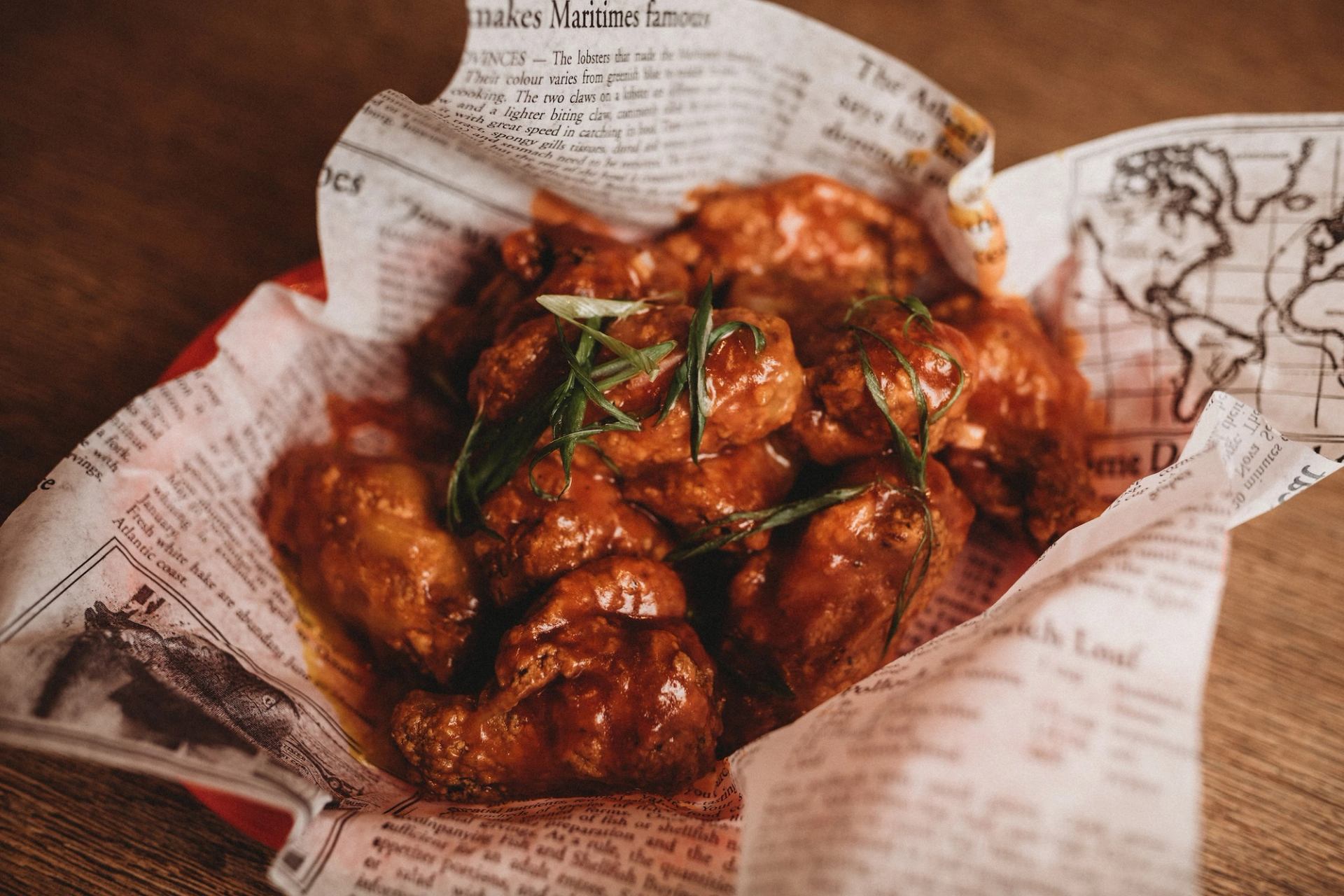 Fried meatballs in paper basket with parsley garnish and napkins on wooden table.