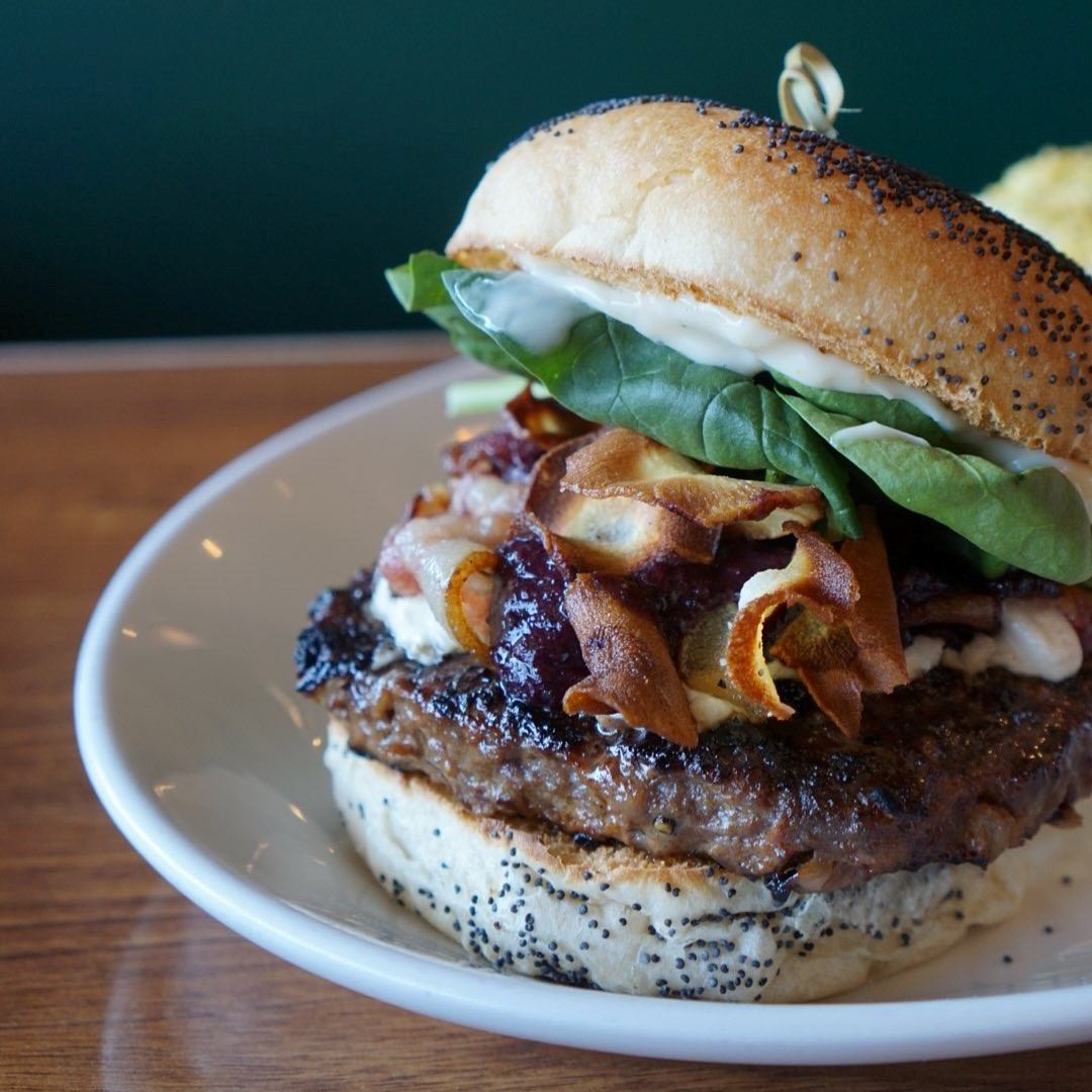 Gourmet burger with bacon, lettuce, and onions on a poppy seed bun.