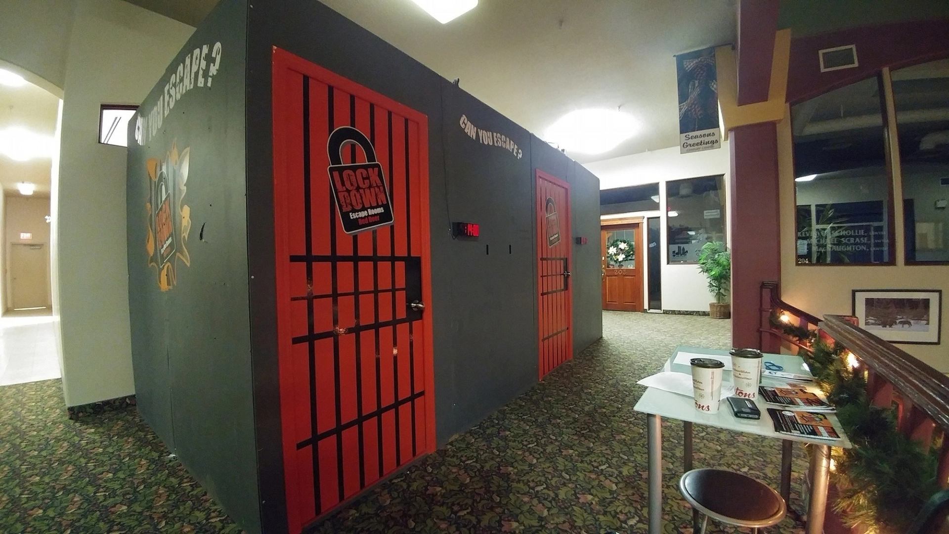 Indoor hallway with Lockdown escape room doors and small table holding coffee cups.