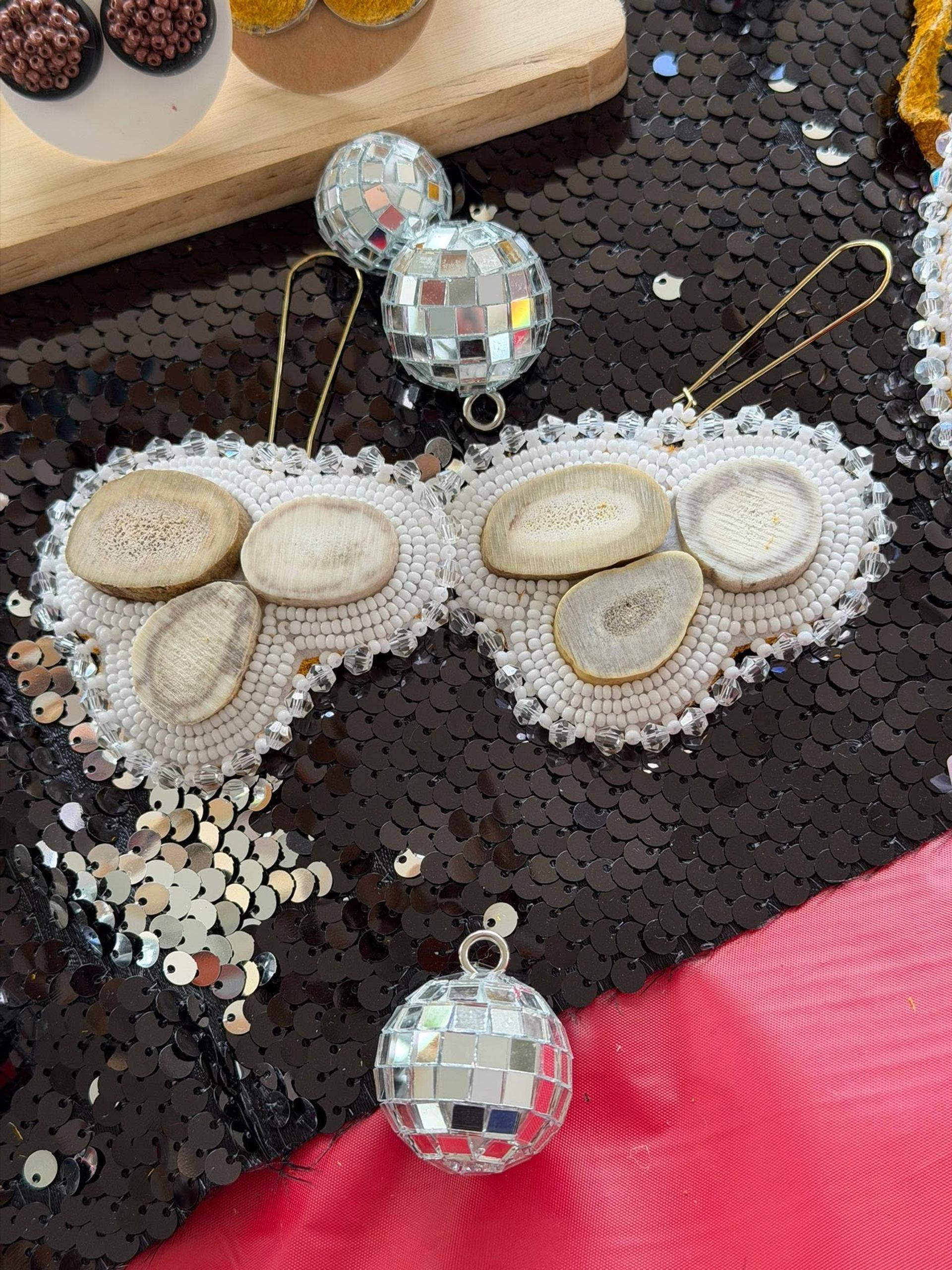 Beaded white accessory with wooden pieces beside small mirrored disco balls on sequins.