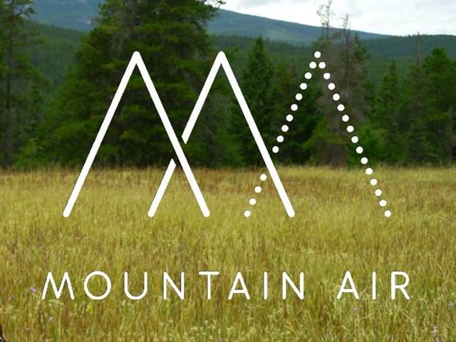 Mountain Air logo over grassy field with trees and mountains in background.
