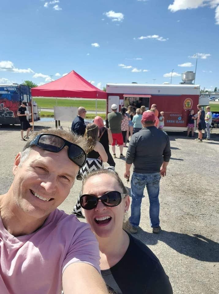 Two people take a selfie near a line at a red food truck.