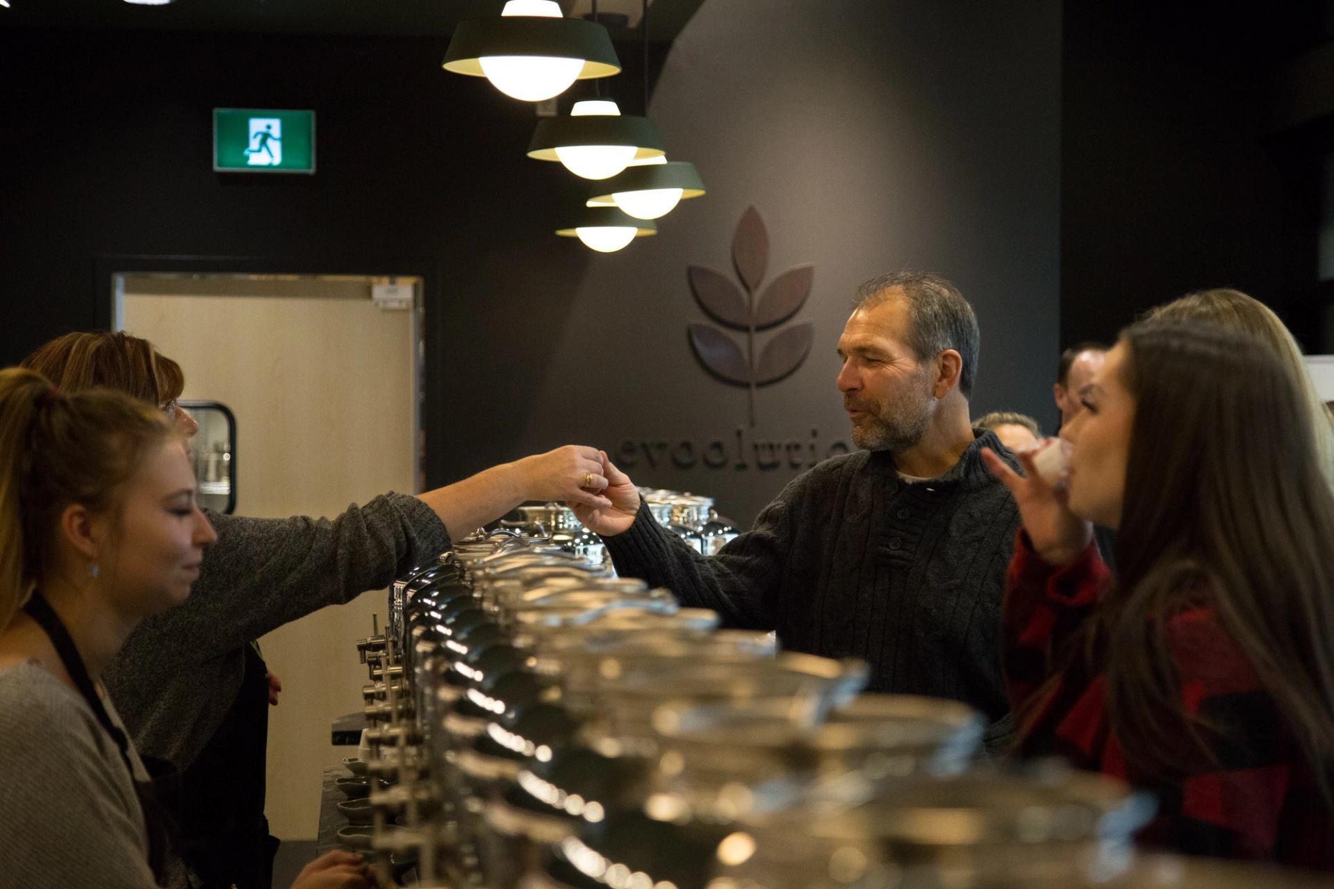People sampling products at a counter in a modern store with “woodstock” logo on the wall.