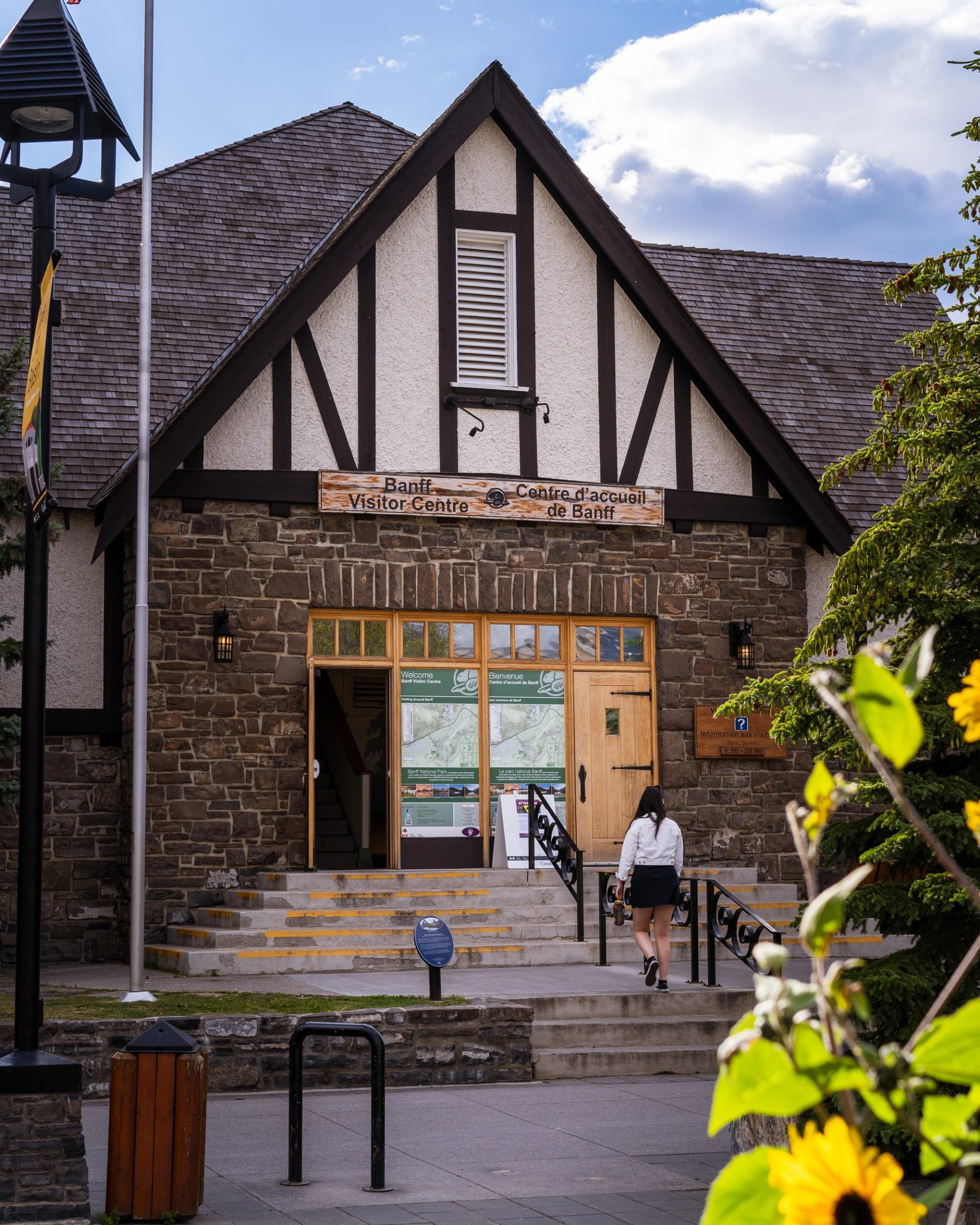 Rustic Banff Visitor Centre with stone and timber design, steps, and flowers in foreground.