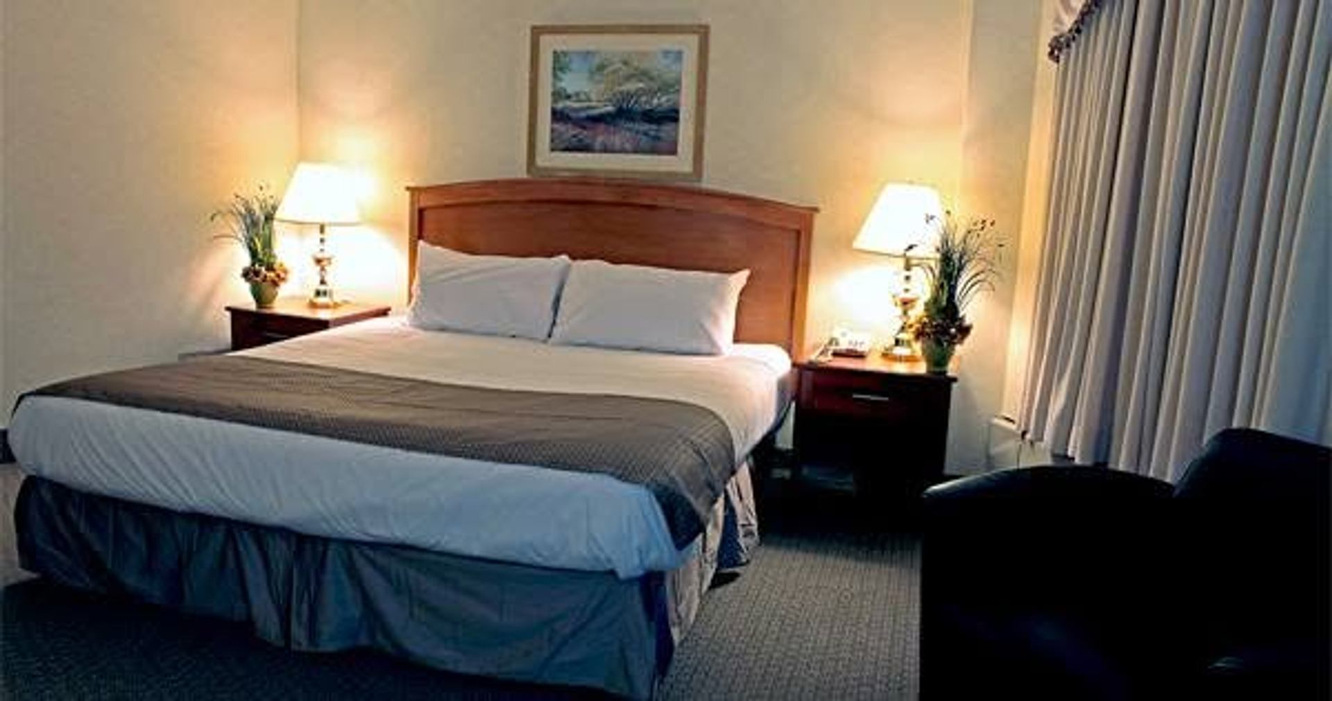Hotel room with a made bed, bedside lamps, framed artwork and closed curtains.