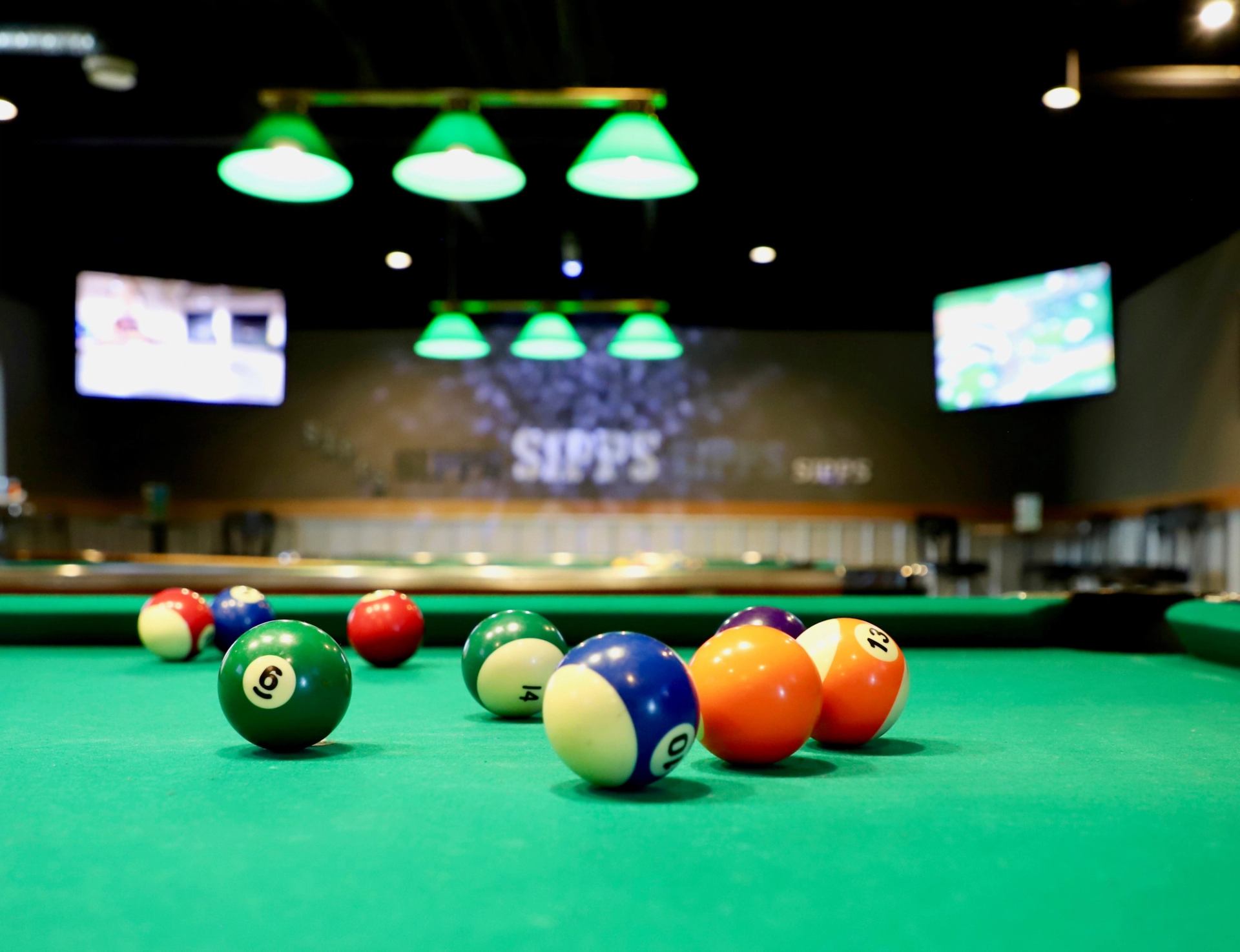 Pool balls on green felt table under lights, SIPPS sign on back wall.