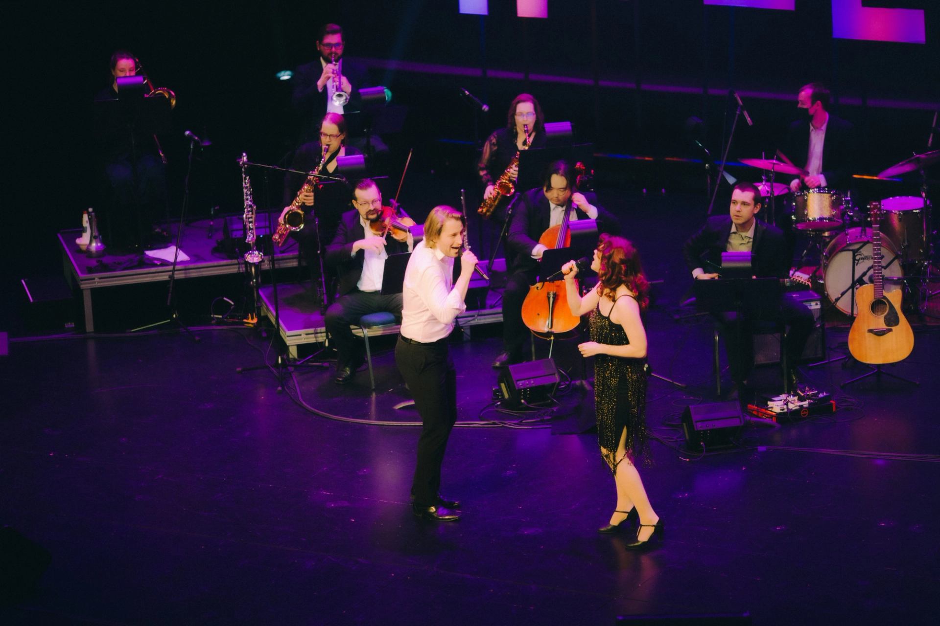 Orchestra stage performance with musicians playing saxophones, violin, trumpet, and upright bass und.