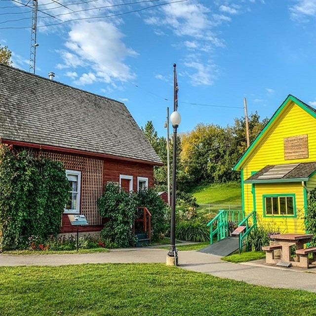 Park buildings with a yellow house, walkway, and green fence under a blue sky.
