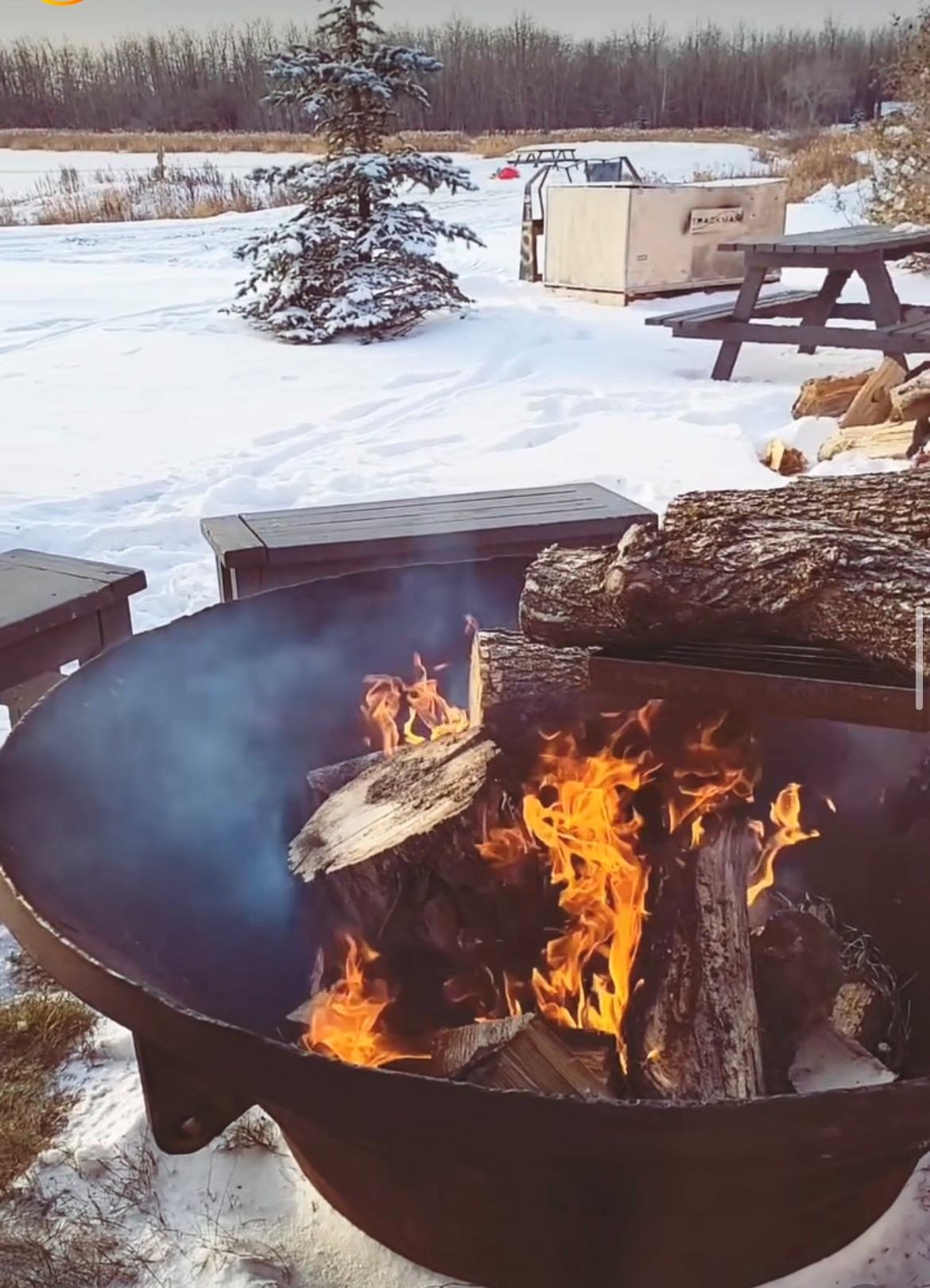 Fire pit flames burning on a circular metal fire bowl at an outdoor golf club.