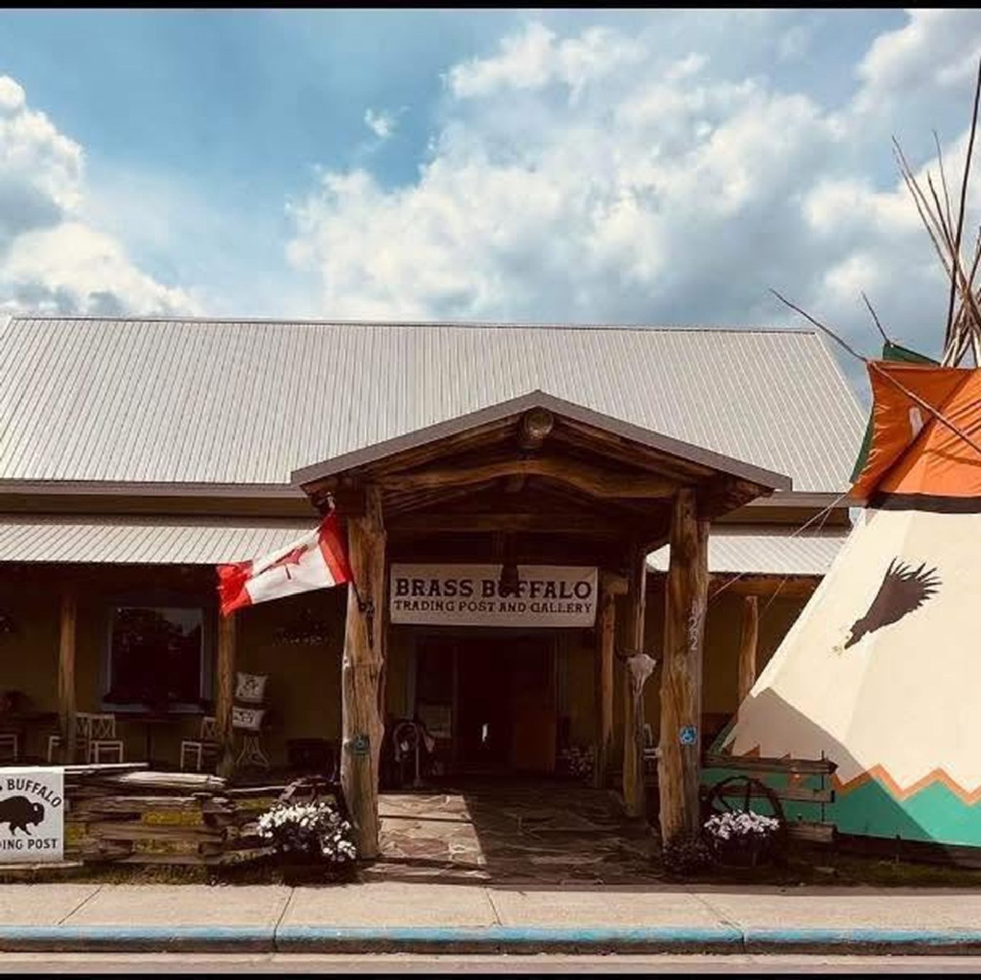 Trading post entrance with Canadian flag, Brass Buffalo sign and painted tipi beside building.