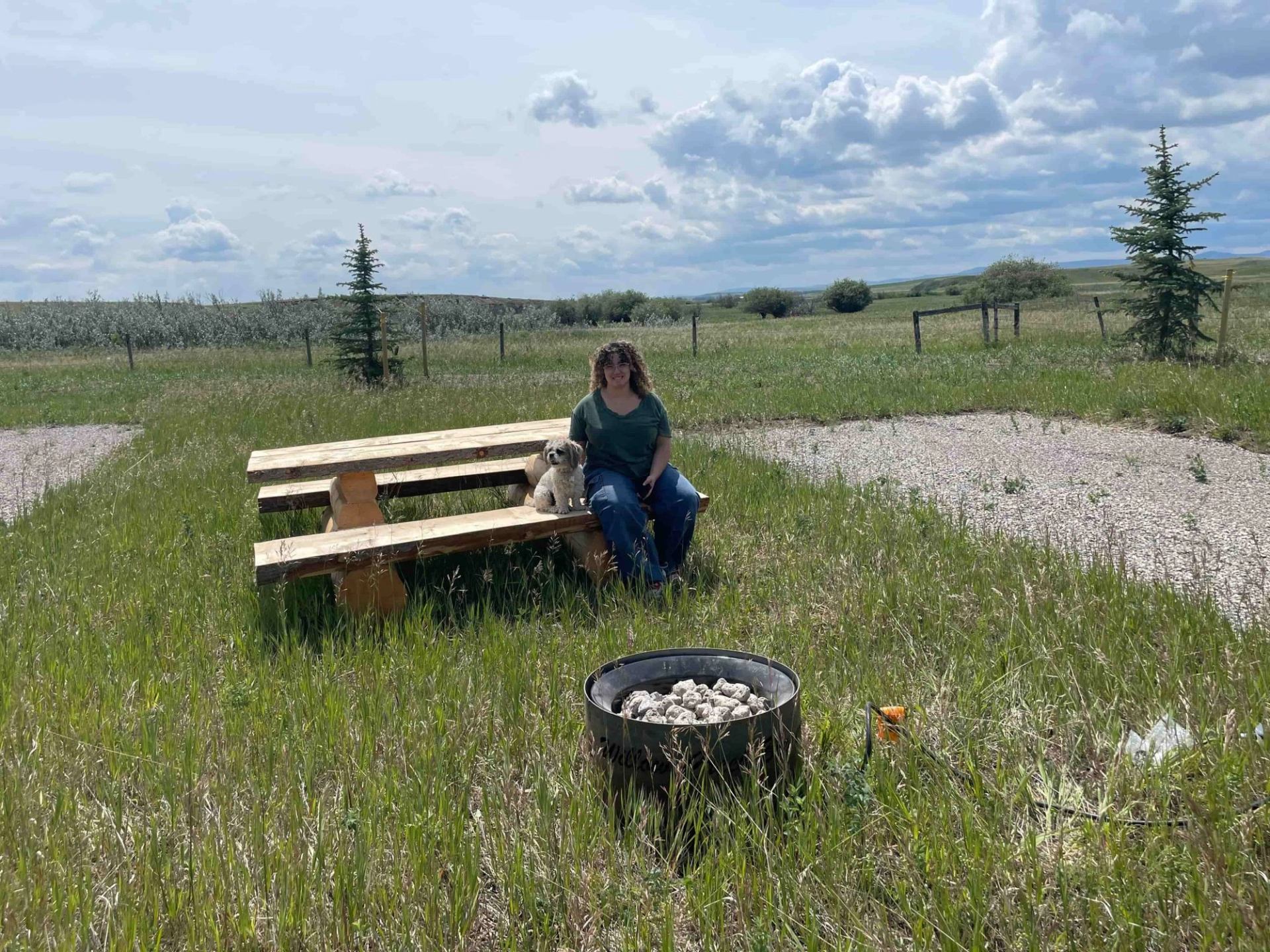 Person seated at picnic table near fire pit in grassy field at Willow Creek Campground.
