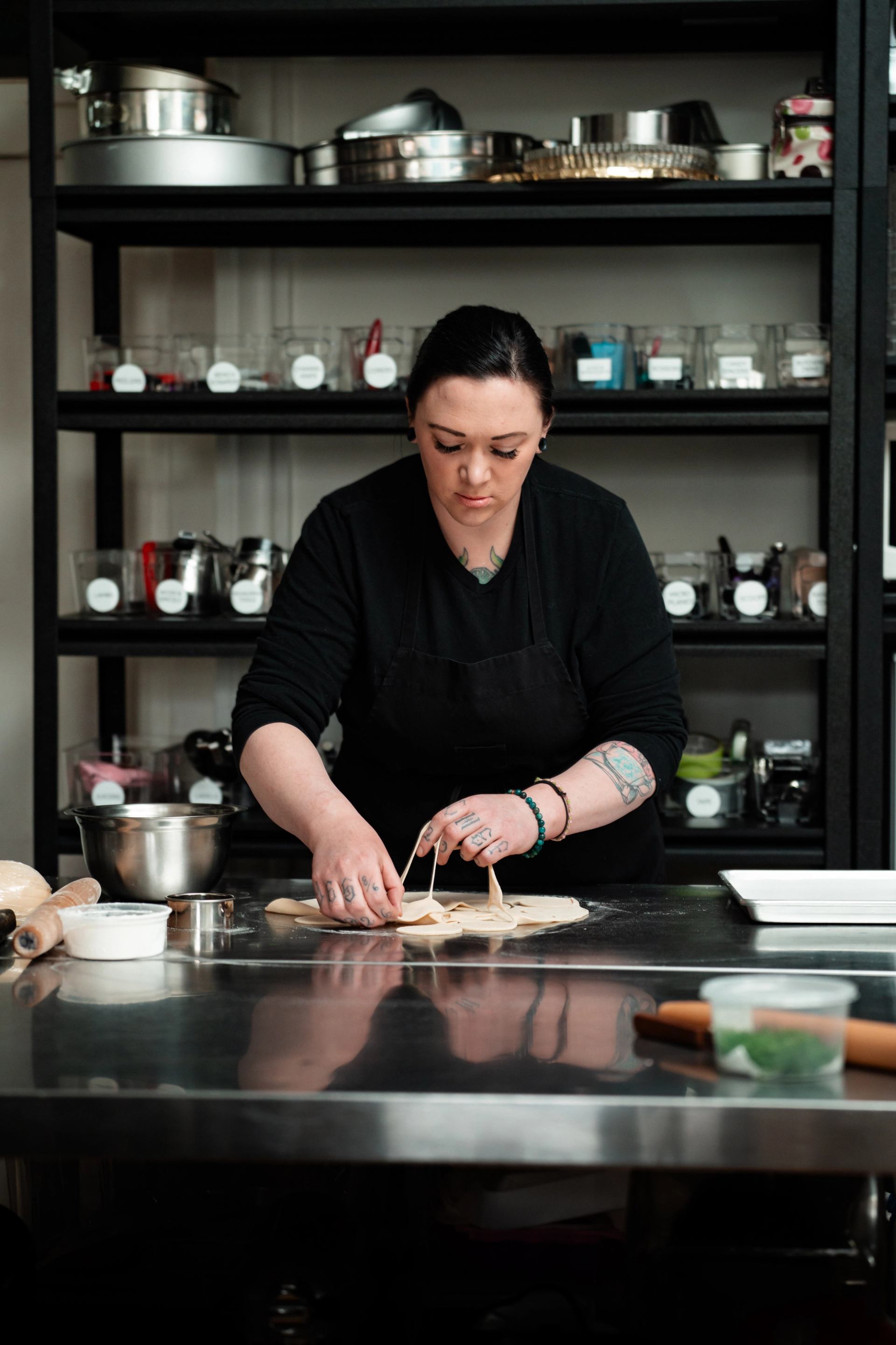 A chef carefully shapes fresh dough at a stainless steel prep station.