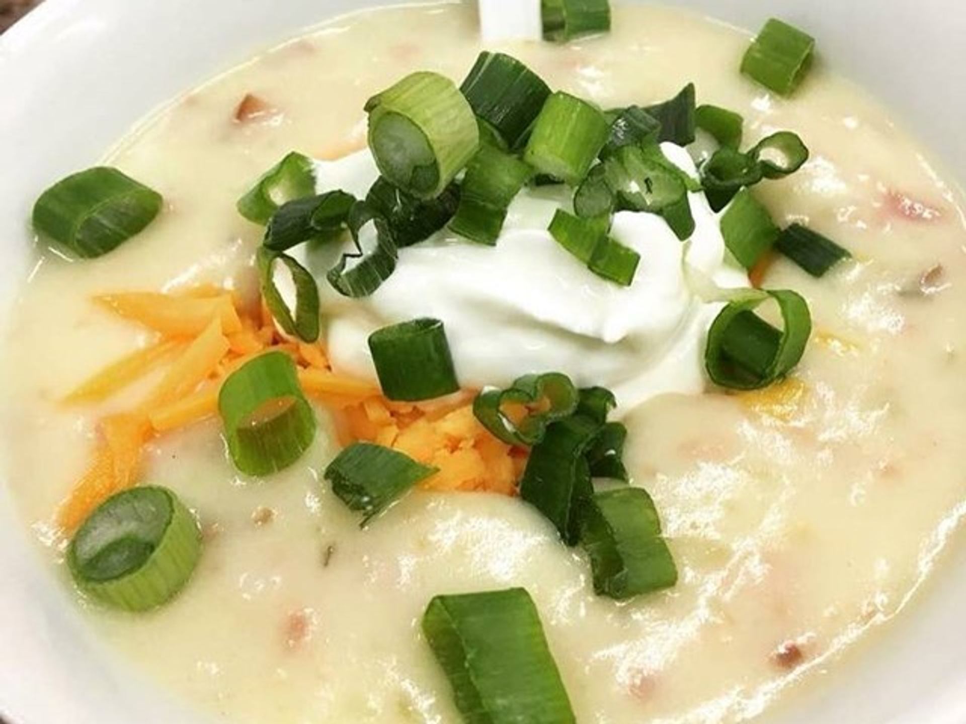 Close-up of creamy soup topped with sour cream, green onions and shredded cheese.