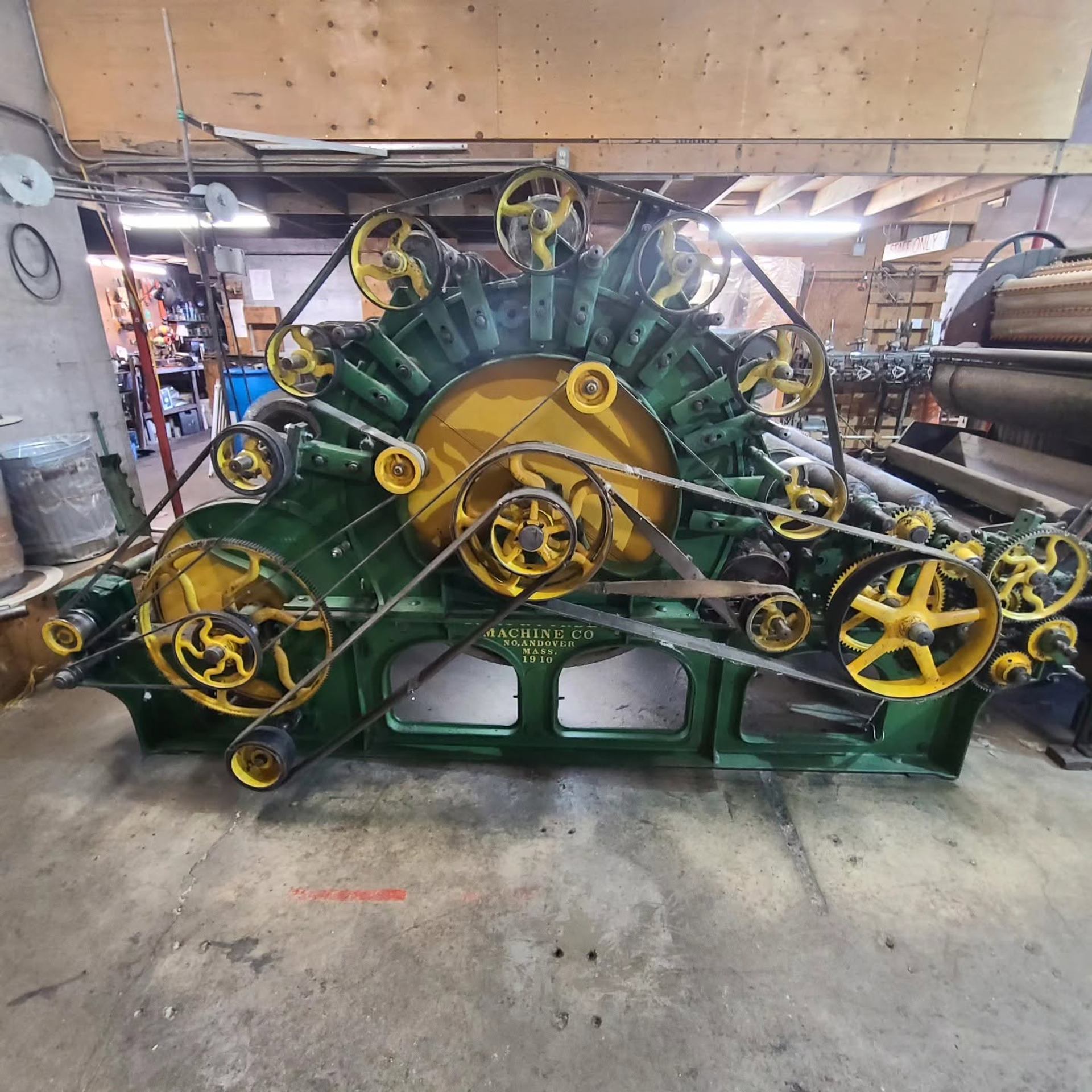 Large green and yellow industrial machine with multiple belts and gears in workshop.